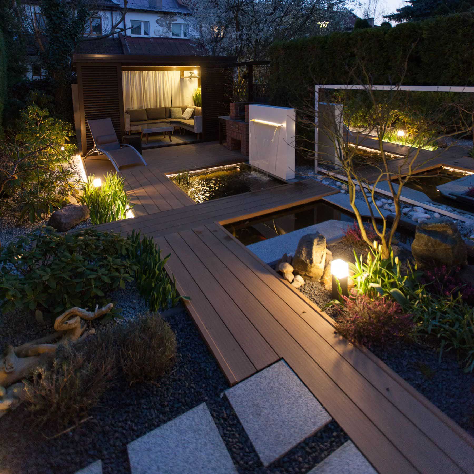 A modern backyard with wood pathways, water features, and a small covered living space.