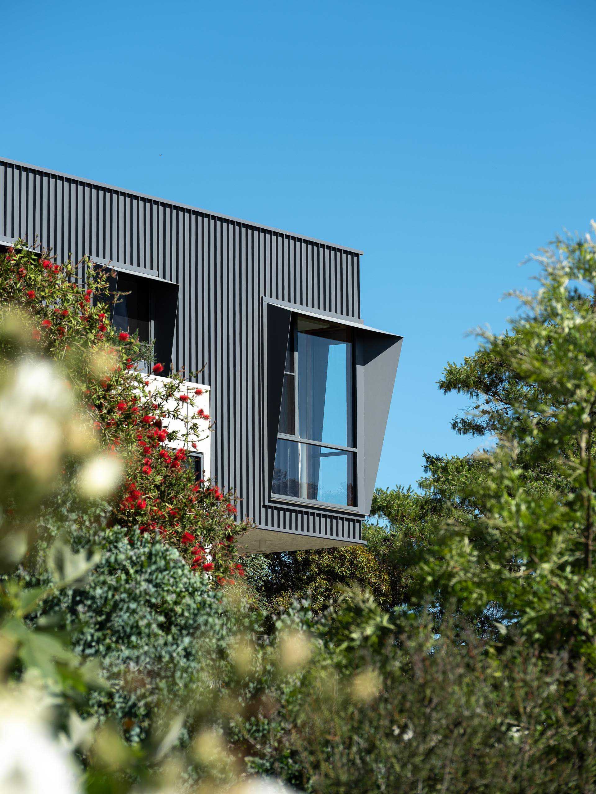 The modern black metal exterior of this home has angled window frames that protrude away from the windows, blocking the sun and offering a shaded interior.