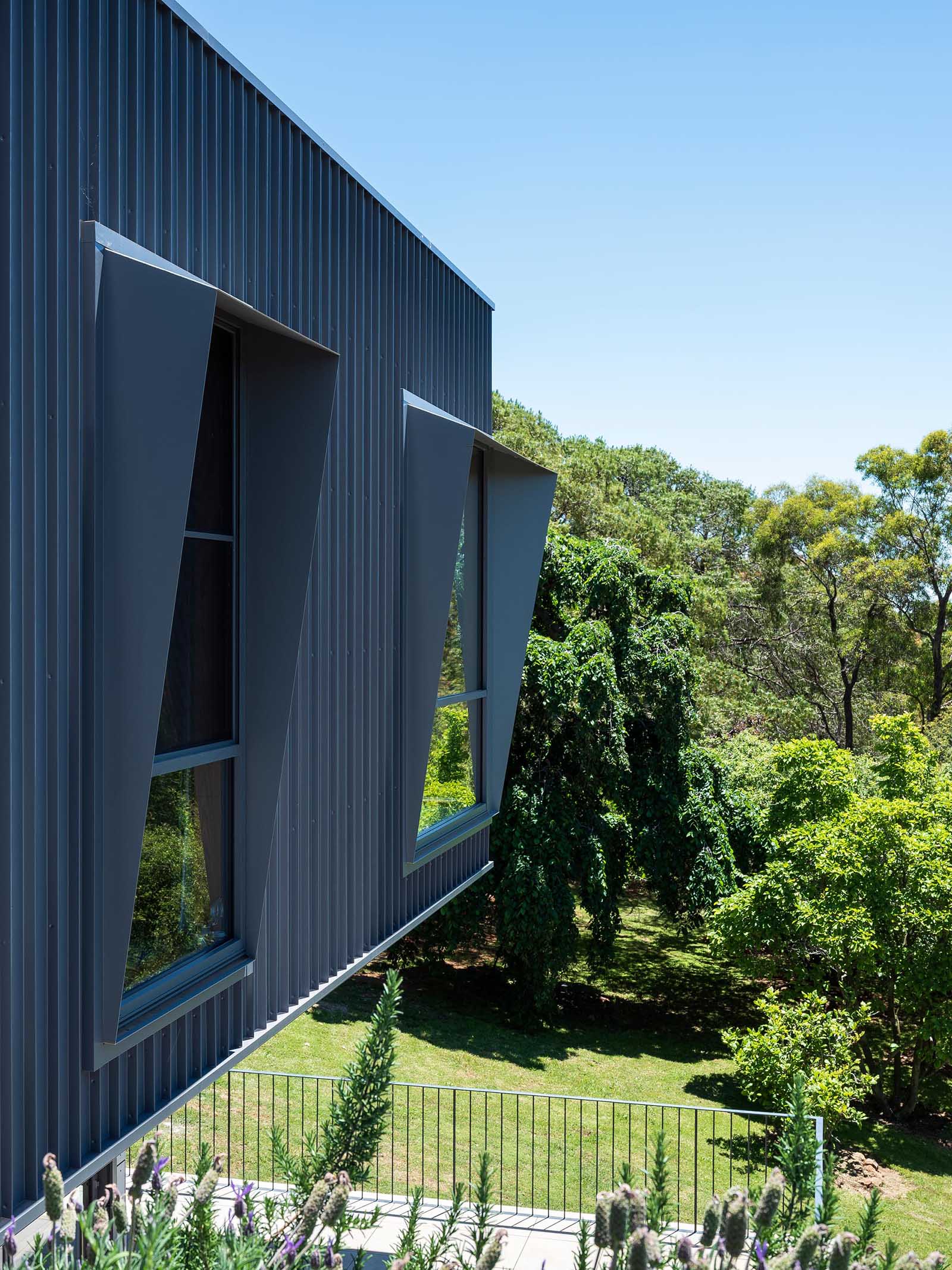 The modern black metal exterior of this home has angled window frames that protrude away from the windows, blocking the sun and offering a shaded interior.