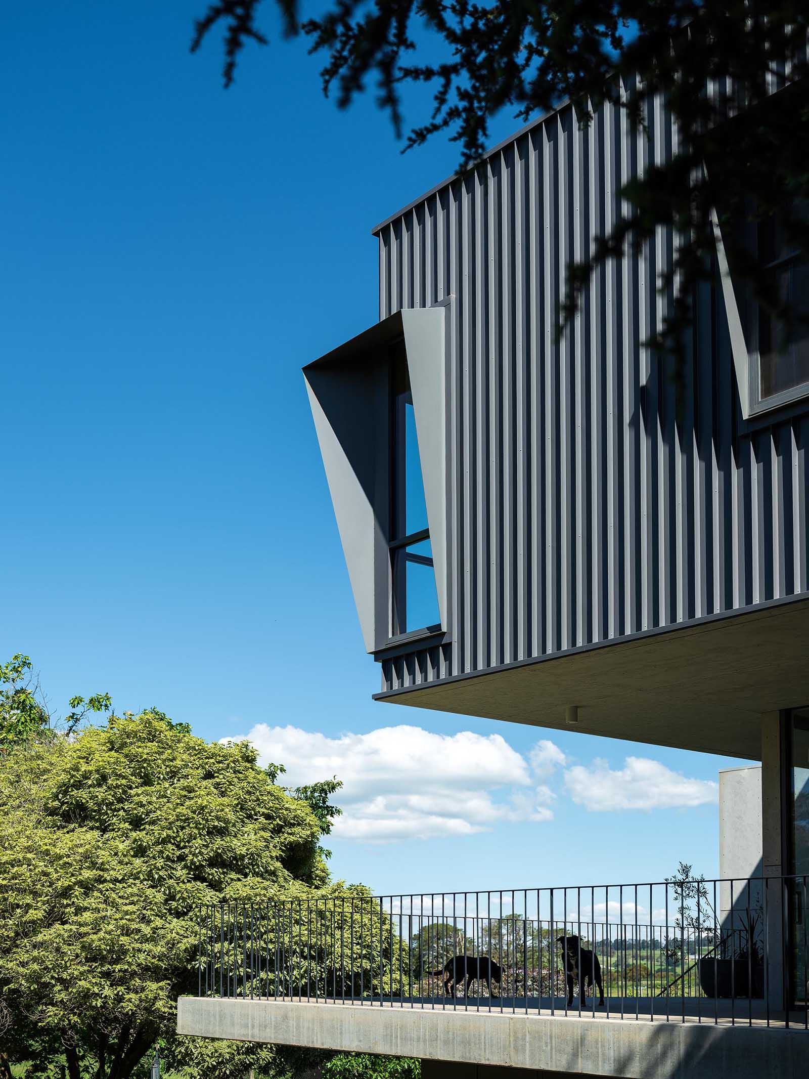 The modern black metal exterior of this home has angled window frames that protrude away from the windows, blocking the sun and offering a shaded interior.