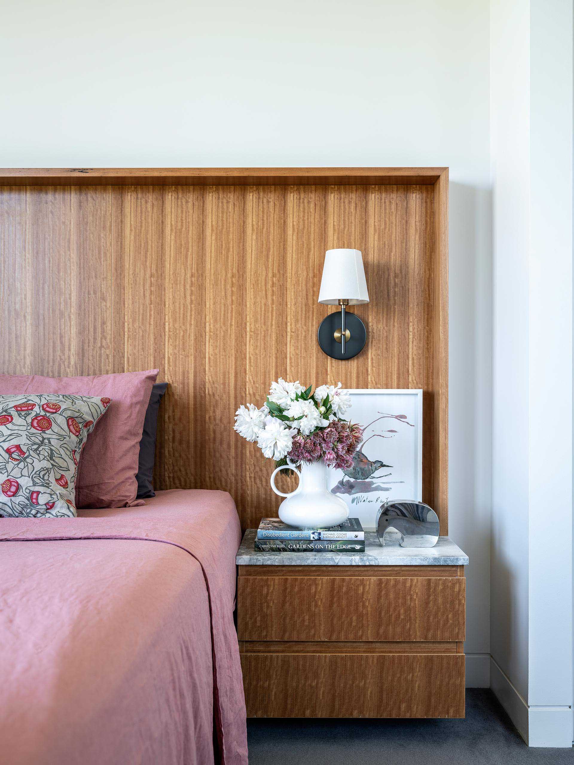 In this modern bedroom, a wide wood headboard incorporates a floating bedside table.