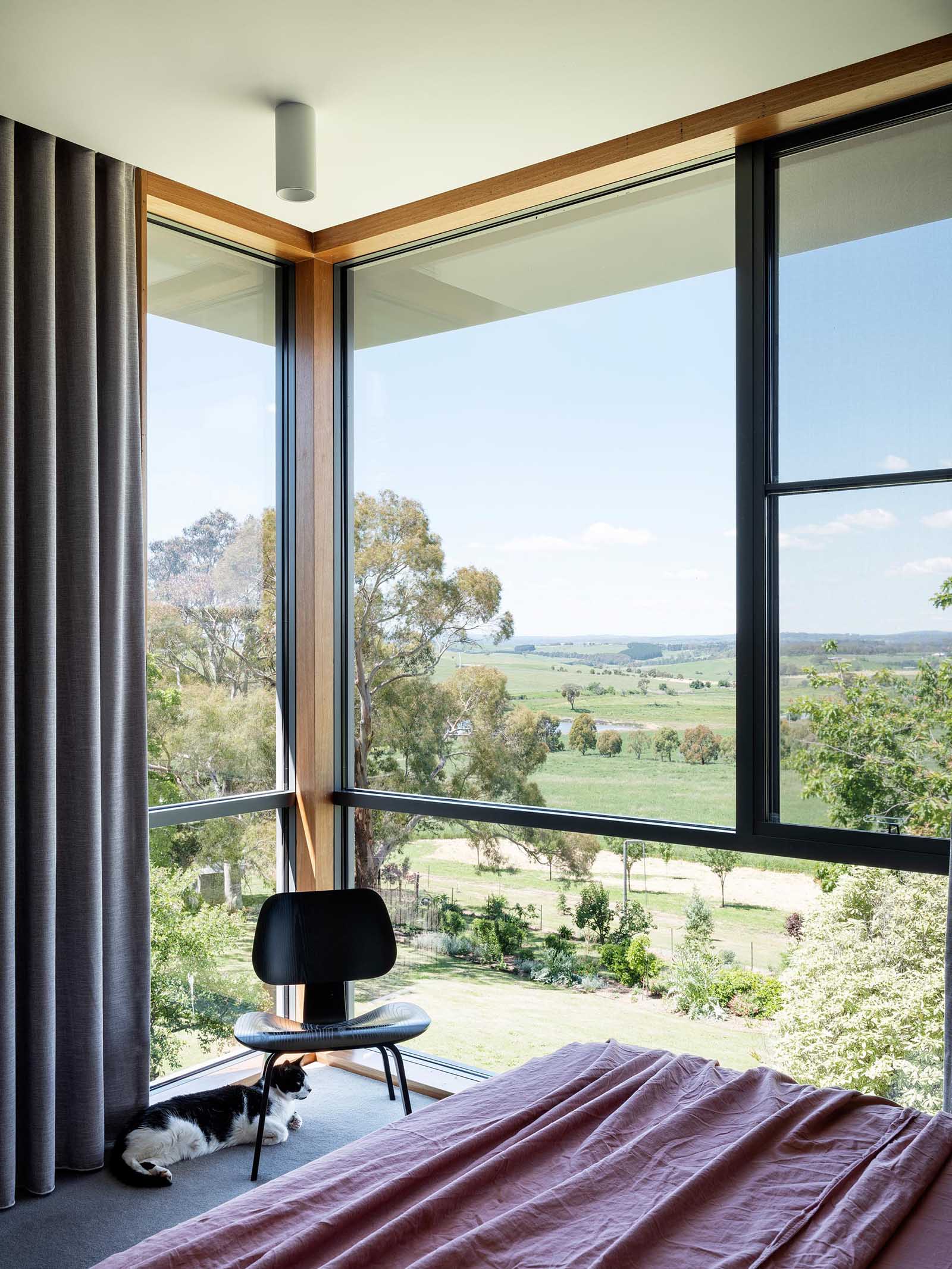 This modern bedroom is filled with an abundance of natural light from the corner windows, which also provide a scenic rural view.