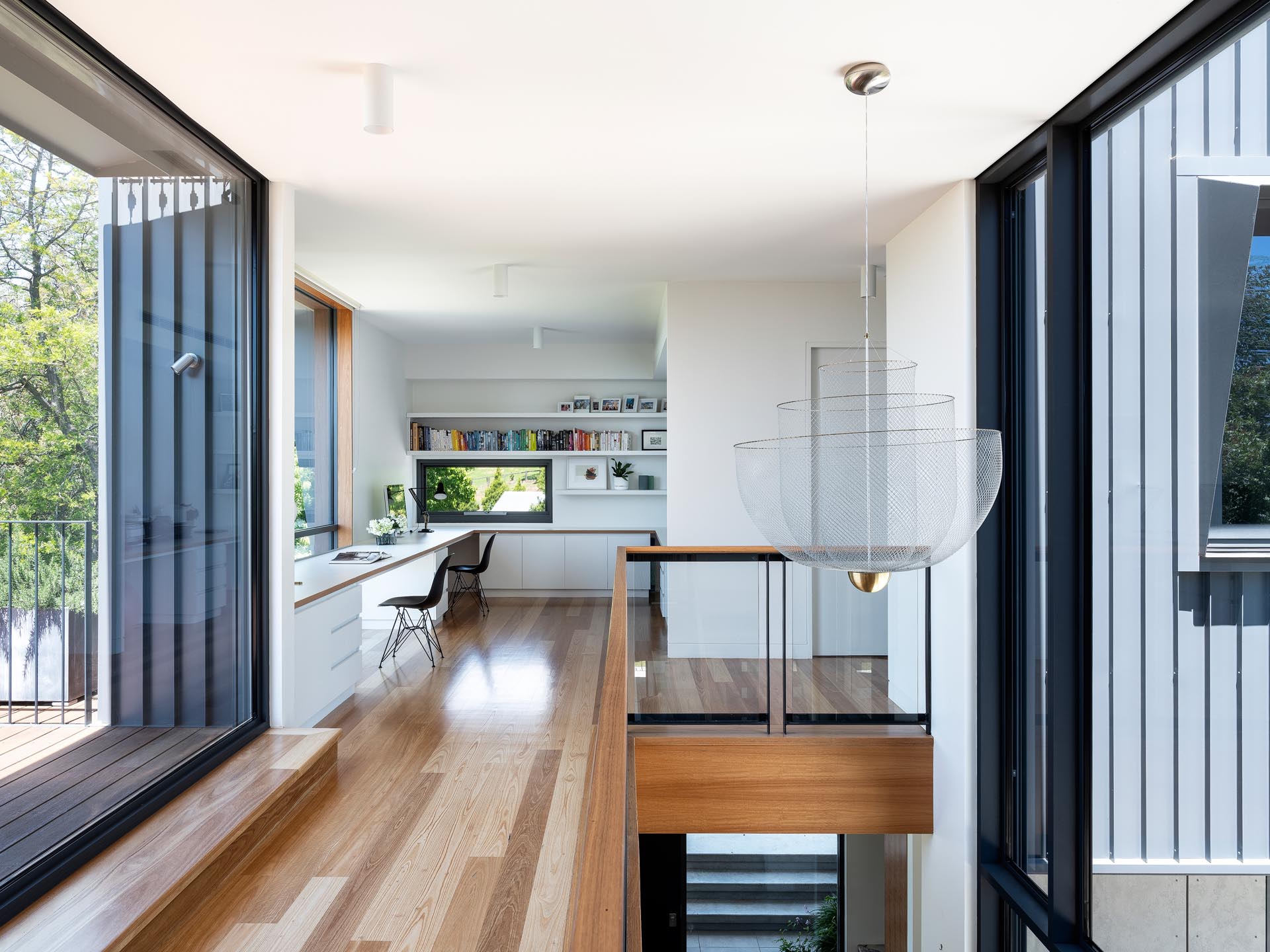 At the top of the stairs in this modern home, is a custom-designed office space that has white shelving, a long desk for two, and plenty of storage.