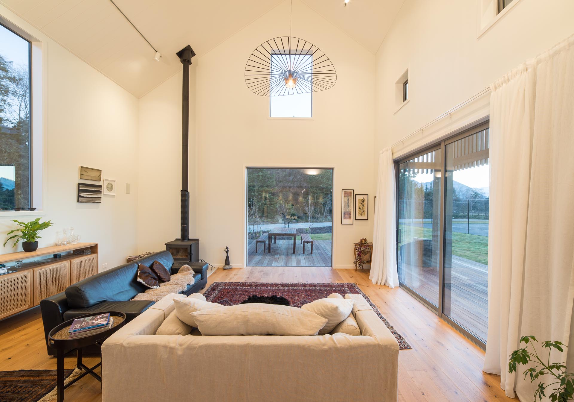 Inside this modern barn-inspired home, the living room has a sense of openness from the double height ceiling, as well as the doors that open to the wood deck outside.