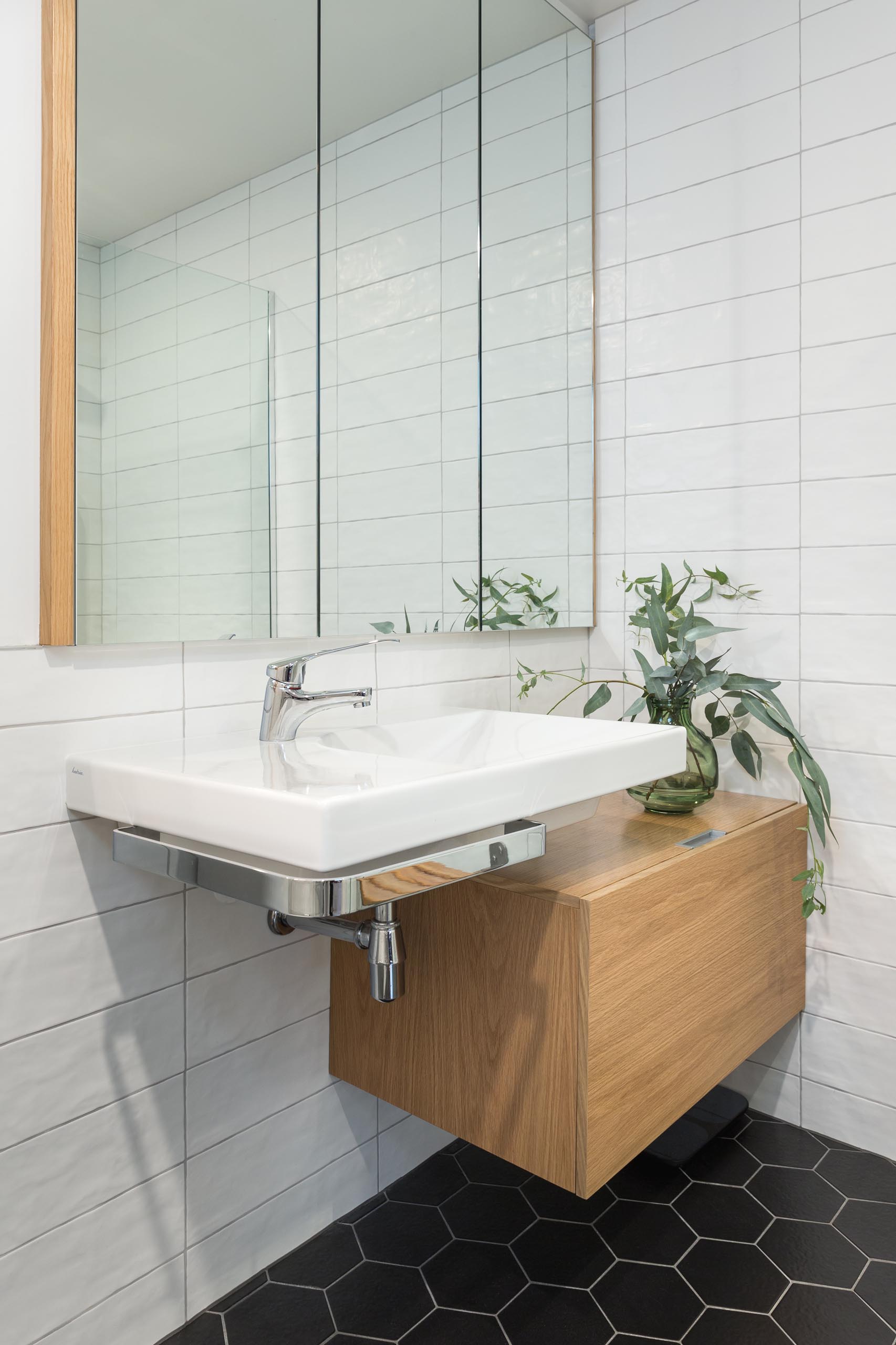 In this modern bathroom, there's black hexagon tiles on the floor and white rectangular tiles on the walls.