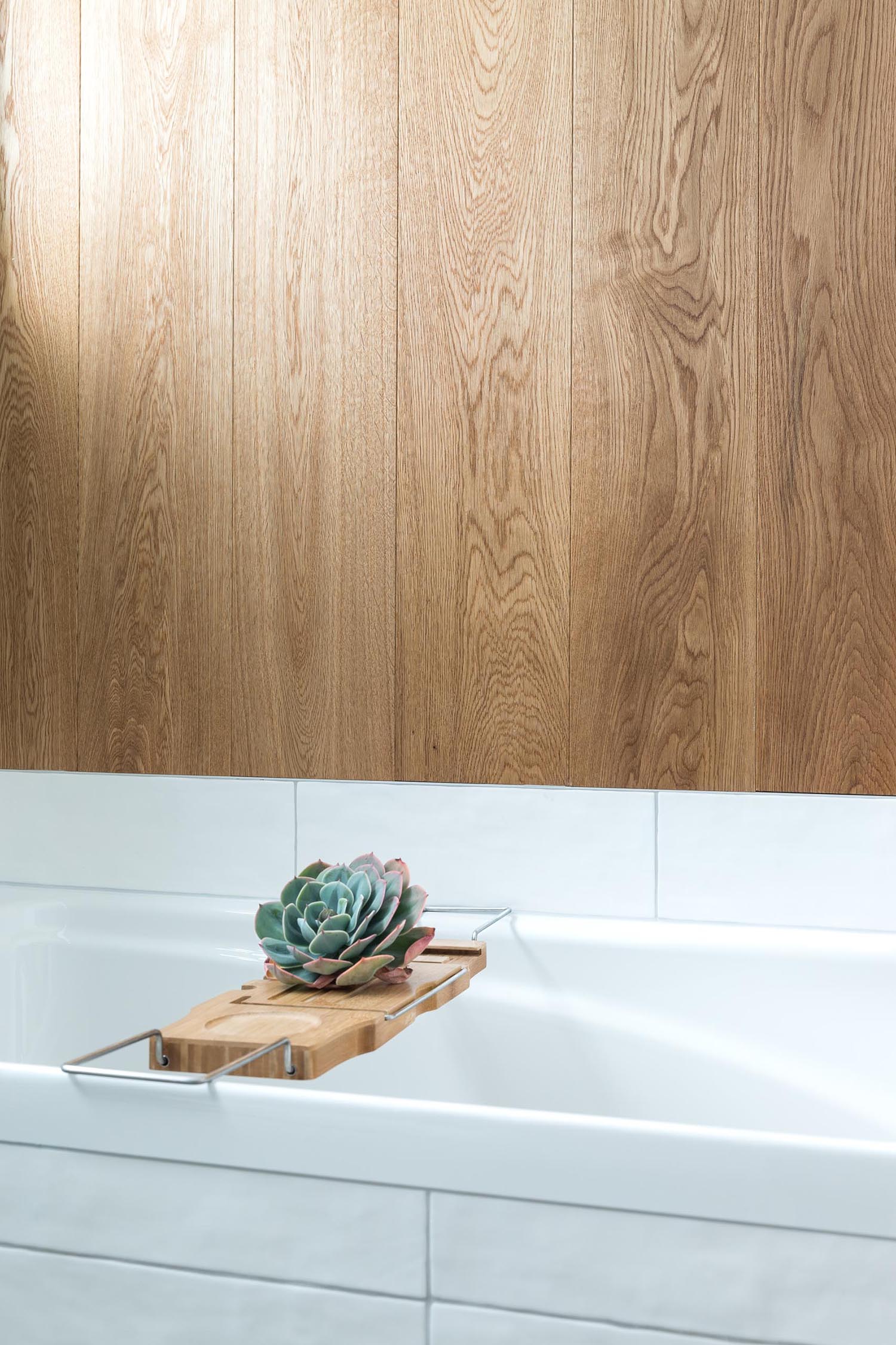 This modern bathroom features a double sink wood vanity, patterned tile flooring, a built-in bathtub, and a wood accent wall.