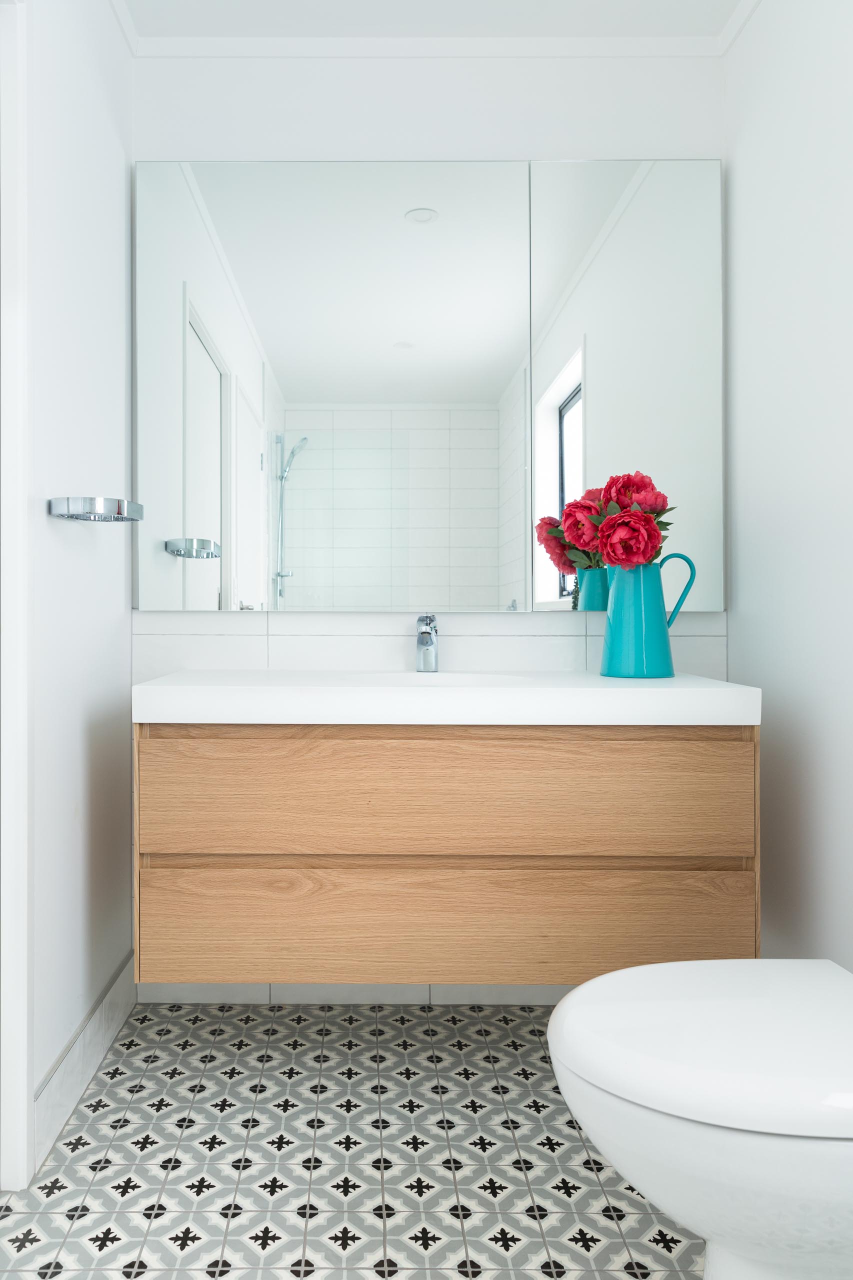 This modern bathroom includes patterned floor tiles, a floating wood vanity, a large mirror, and white wall tiles.