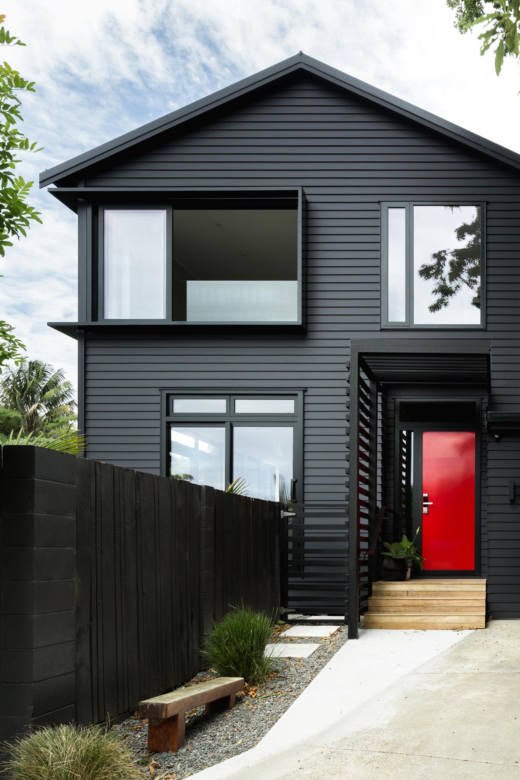 This modern house is in cedar weatherboards, and painted black creating a bold exterior, while the bright red door adds a strong contrasting design element.