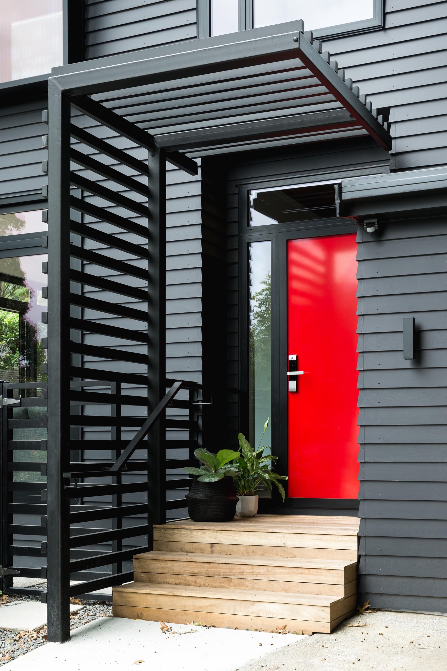 This modern house is in cedar weatherboards, and painted black creating a bold exterior, while the bright red door adds a strong contrasting design element.