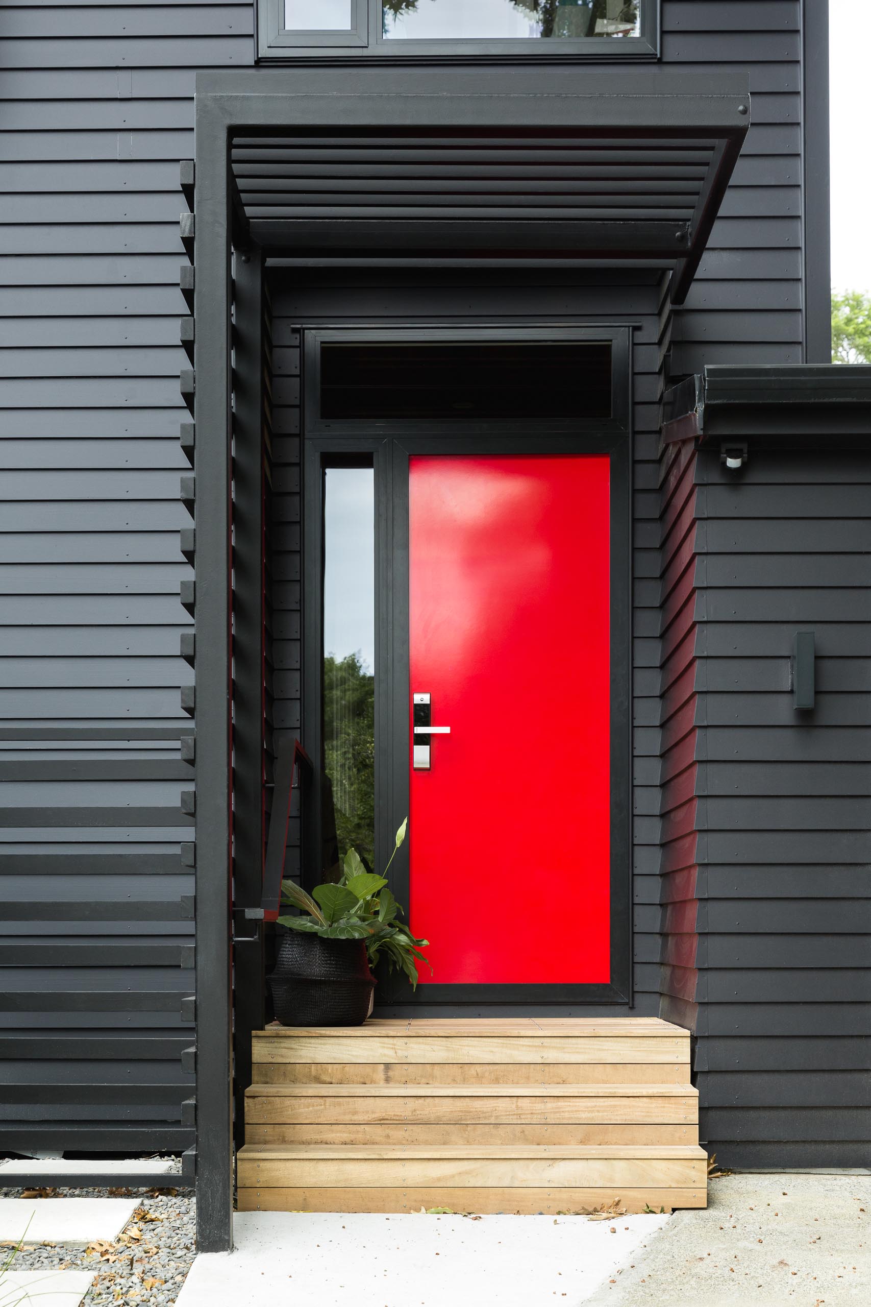 This modern house is in cedar weatherboards, and painted black creating a bold exterior, while the bright red door adds a strong contrasting design element.