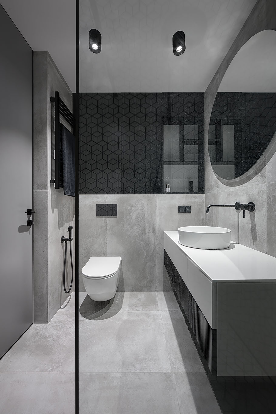 The bathroom includes a white, gray and black interior, with a bright white vanity, concrete wall and floor tiles, white geometric tiles with black grout, and a custom black shelving niche.
