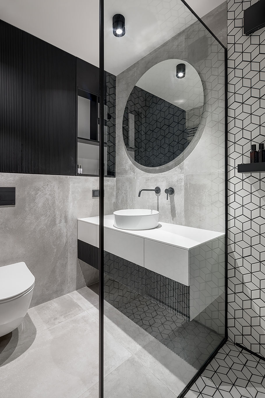 The bathroom includes a white, gray and black interior, with a bright white vanity, concrete wall and floor tiles, white geometric tiles with black grout, and a custom black shelving niche.