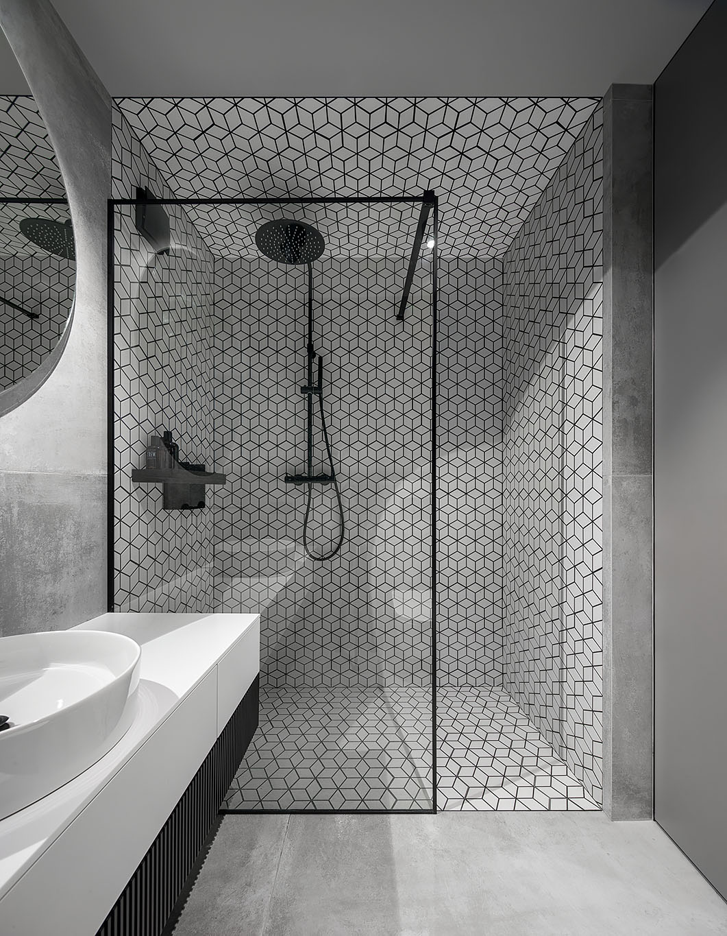 The bathroom includes a white, gray and black interior, with a bright white vanity, concrete wall and floor tiles, white geometric tiles with black grout, and a custom black shelving niche.