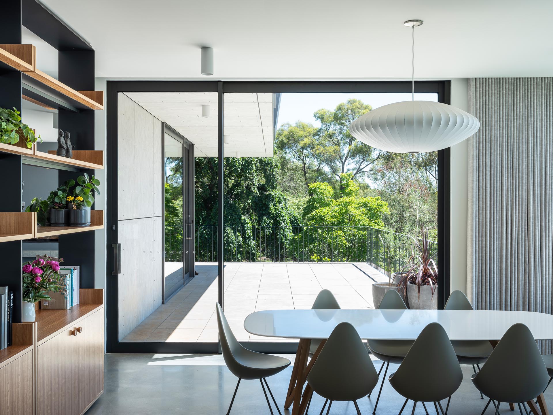 A modern dining room with a custom shelving unit, has access to a deck.