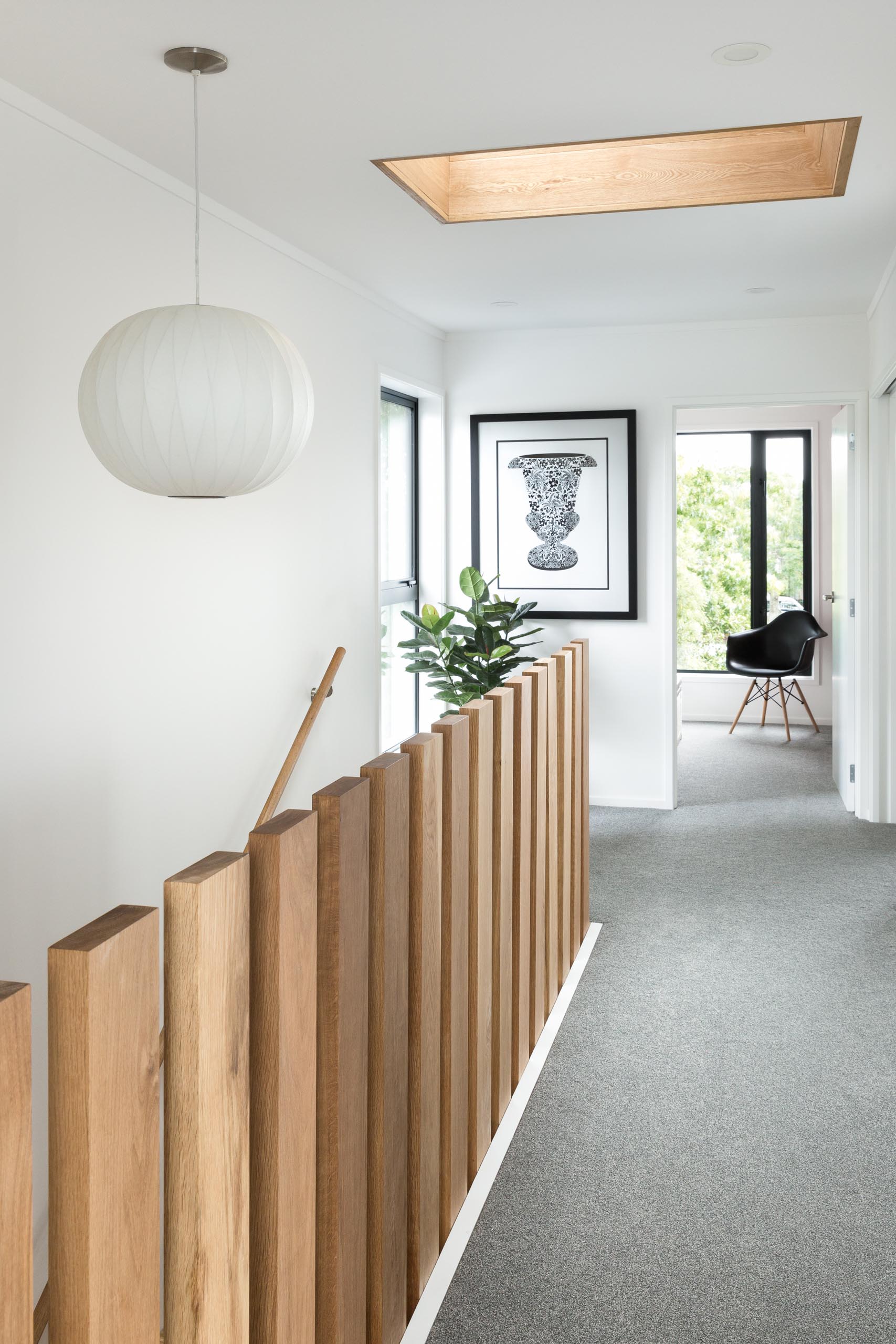 This modern home includes stair balusters are engineered to float above the landing without being tied together. Beyond is a glimpse of the oak tree that the design was inspired by, while the ceiling also features a wood lined skylight adding extra natural light to the stairwell below.