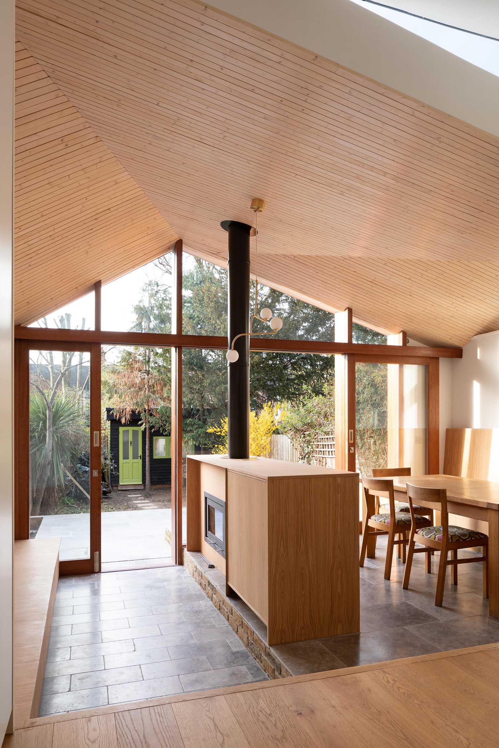 The interior of this new home addition includes an angled ceiling lined with light wood, which creates glimpses of the sky in different directions.