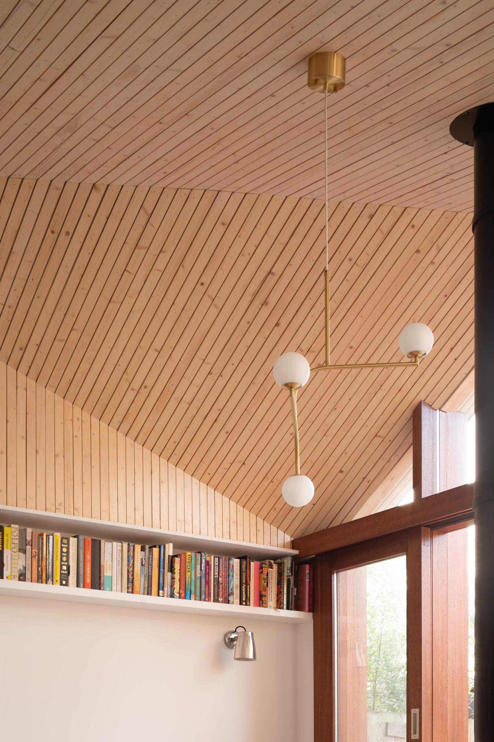 The interior of this new home addition includes an angled ceiling lined with light wood, which creates glimpses of the sky in different directions.