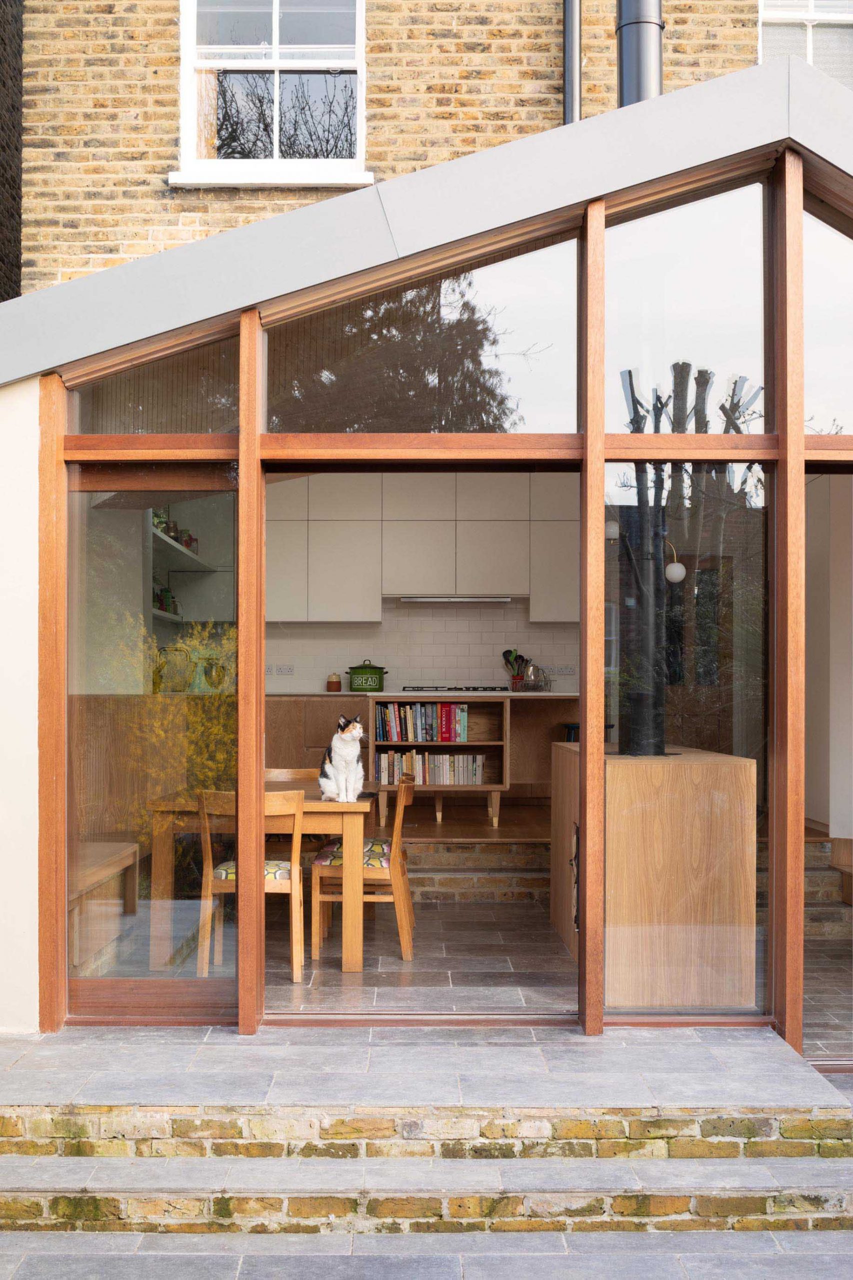 This new home addition has a wall of wood-framed windows, while the form of the roof allows light to get to the back of the interior.