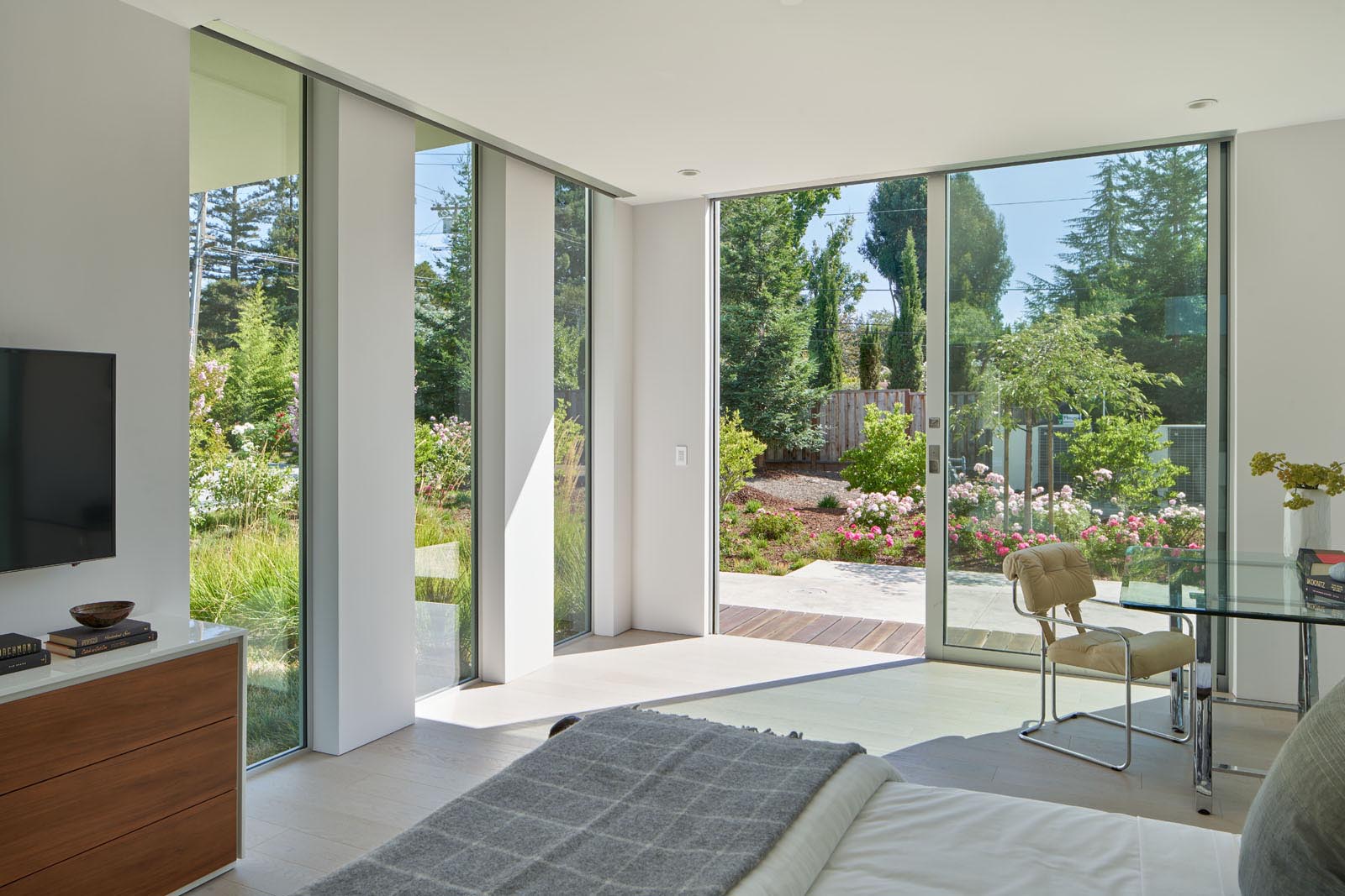 The bedroom has floor-to-ceiling windows and a sliding glass door that opens to a patio and the garden.