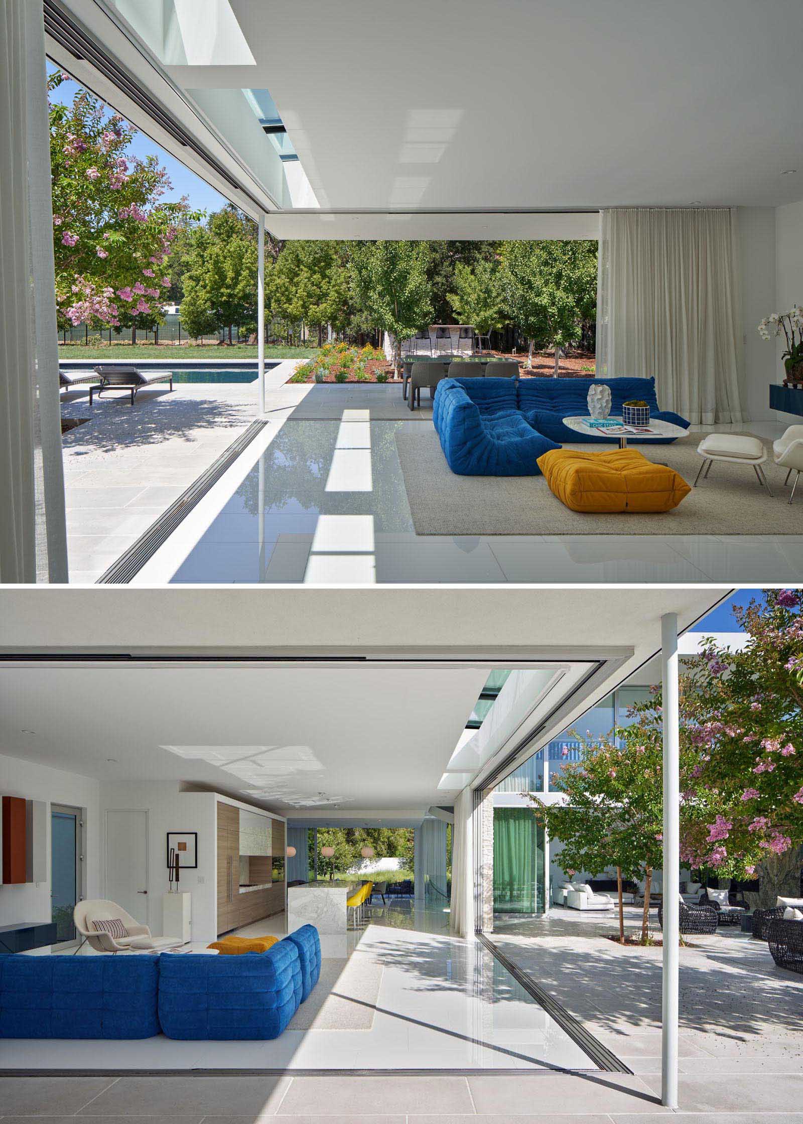 This modern living room has pocketing sliding glass doors that dissolve the boundary between inside and outside. At night, white curtains can be closed for privacy.
