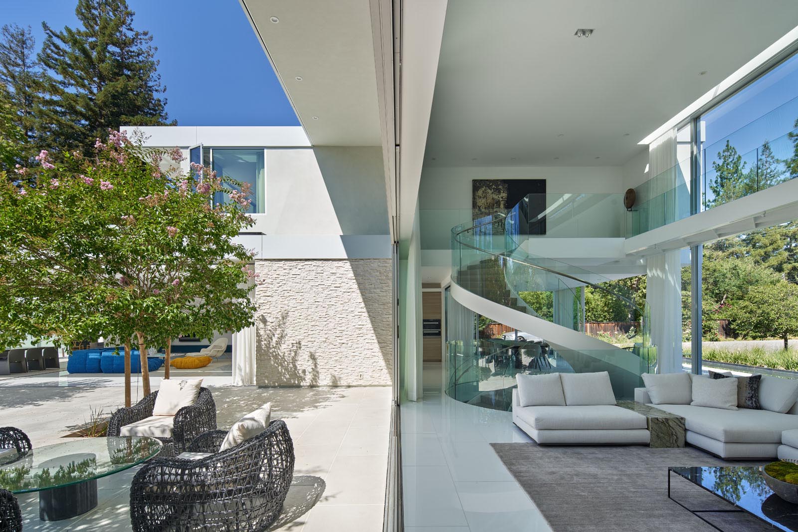 This modern living room has pocketing sliding glass doors that dissolve the boundary between inside and outside. At night, white curtains can be closed for privacy. 