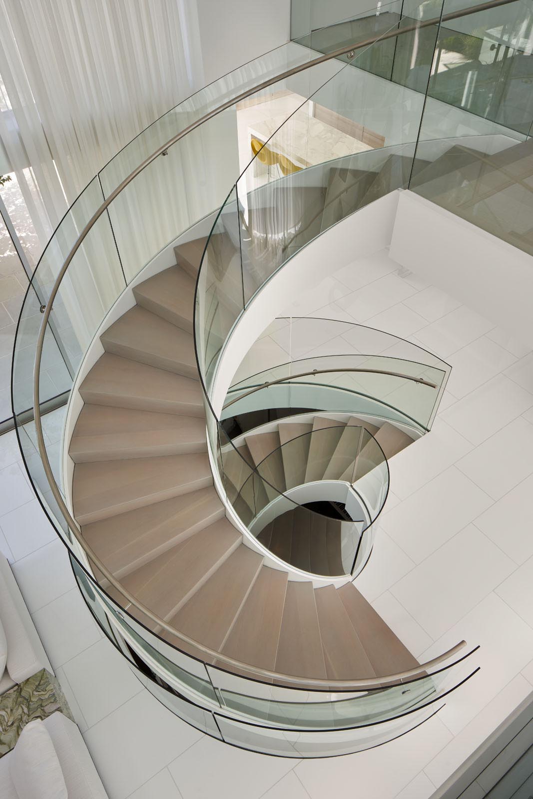 This custom designed spiral staircase includes glass handrails and a steel frame that complements the surrounding white walls.