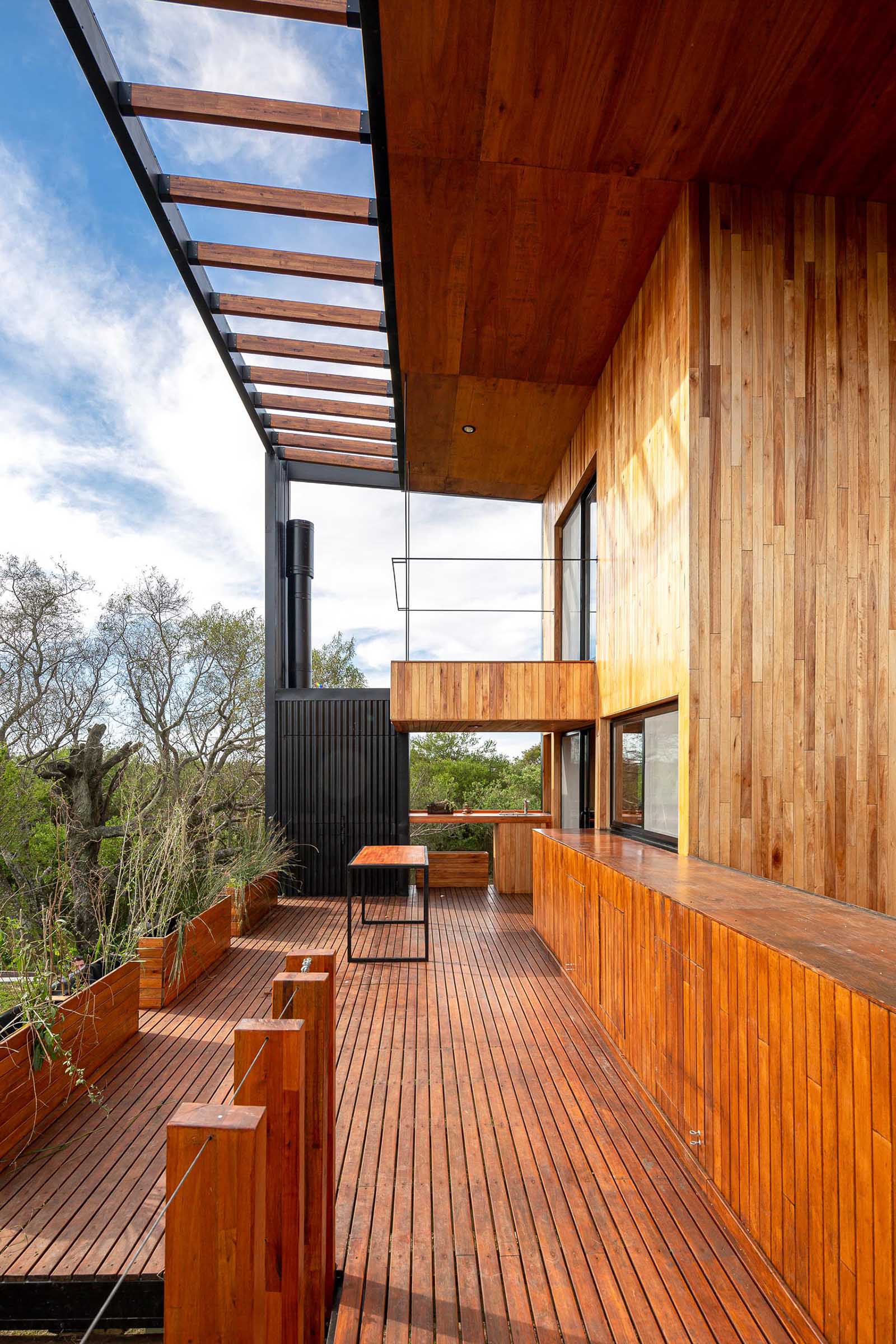 Stairs connect the ground level to the deck of this small house, includes matching wood planters, outdoor dining area, and a small kitchen space with a sink.