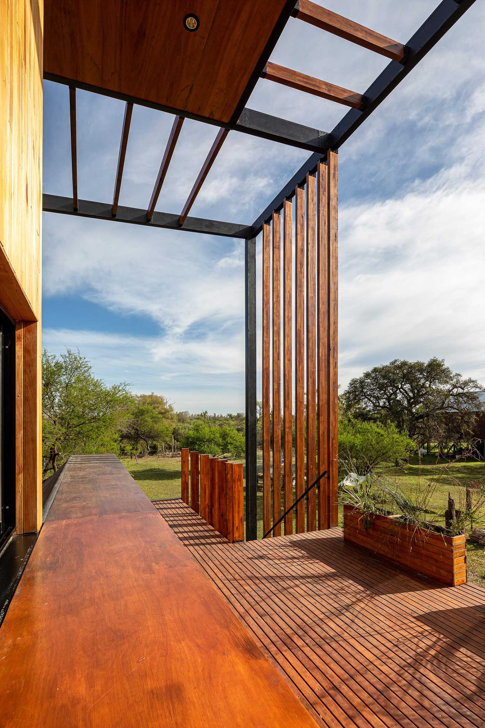 Stairs connect the ground level to the deck of this small house, includes matching wood planters, outdoor dining area, and a small kitchen space with a sink.