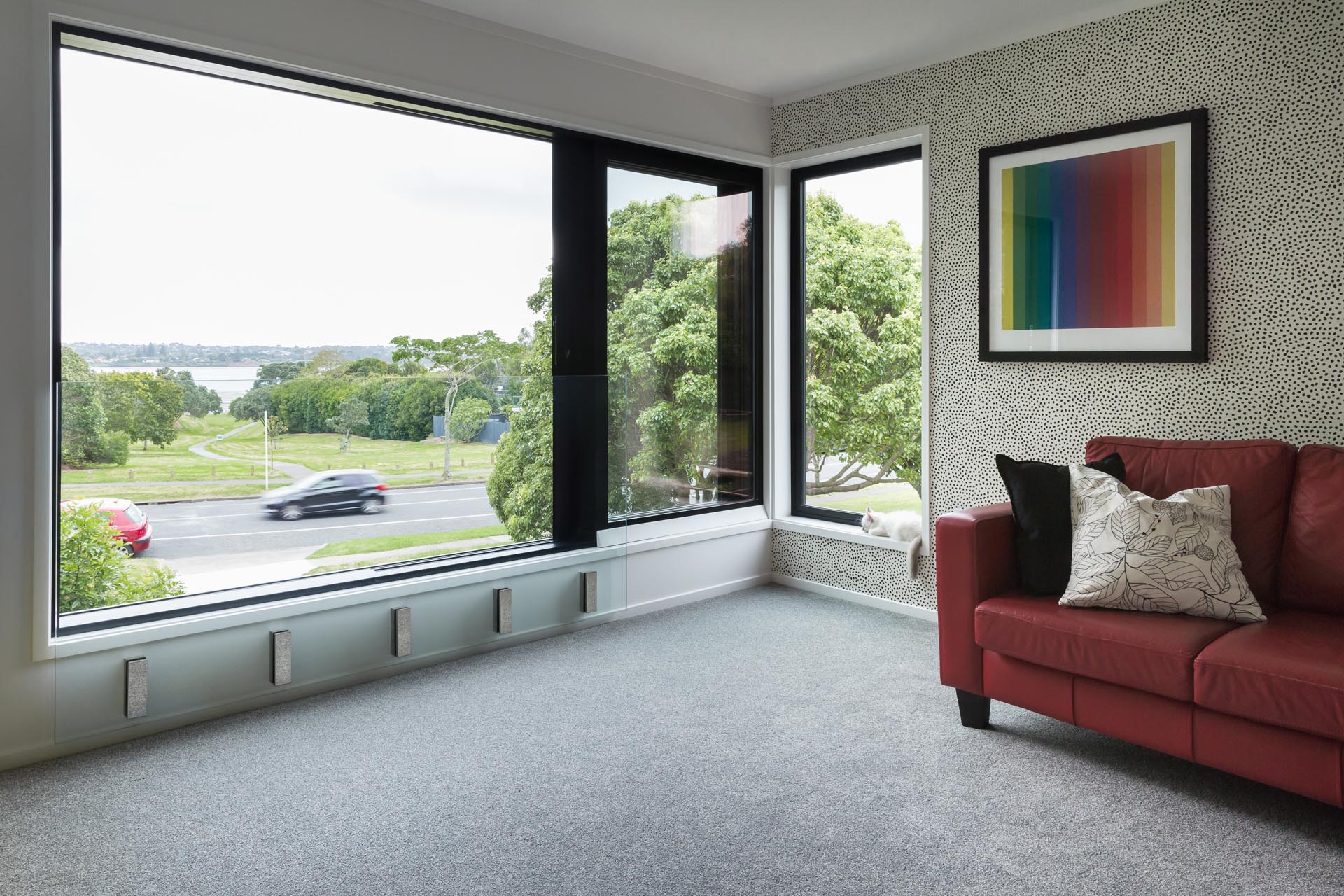 This modern living room includes white walls, grey carpet, dot patterned accent wall, and bold black window frames.