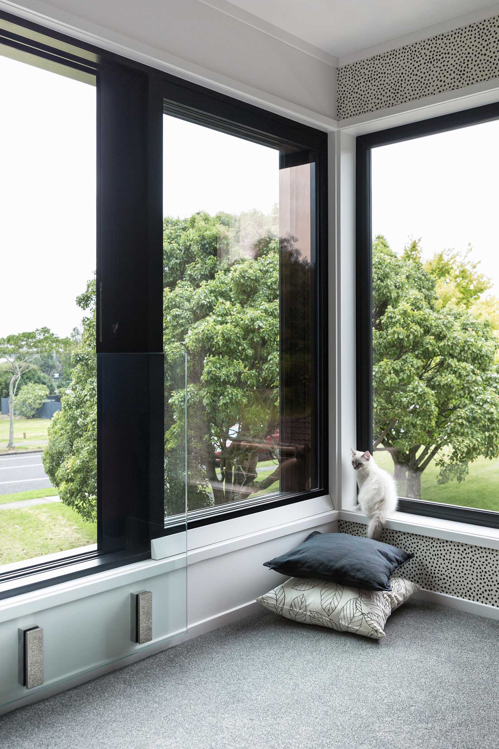 This modern living room includes white walls, grey carpet, dot patterned accent wall, and bold black window frames.