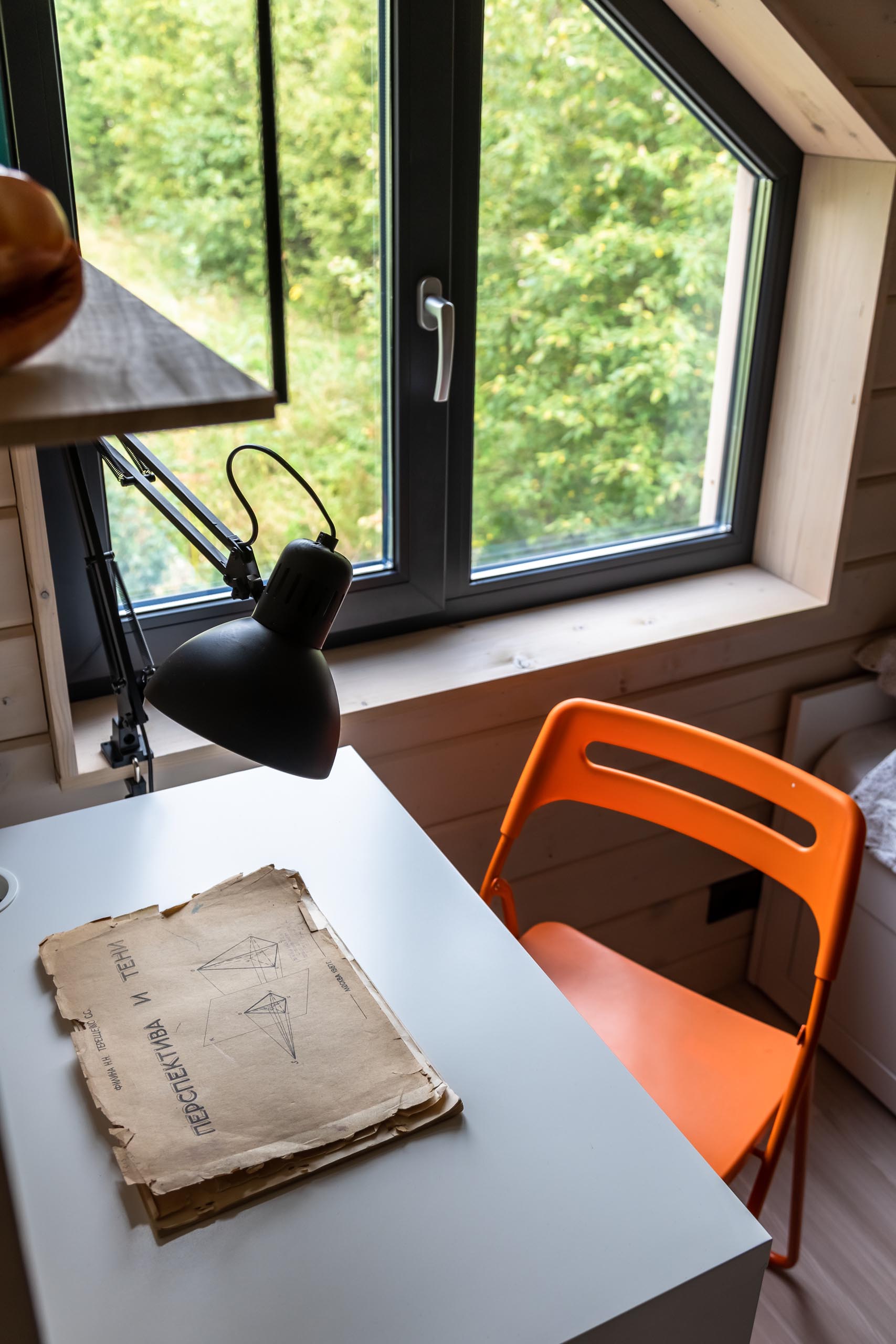 A modern kid's bedroom with tongue and groove wood siding, a white desk, black light, and orange chair.