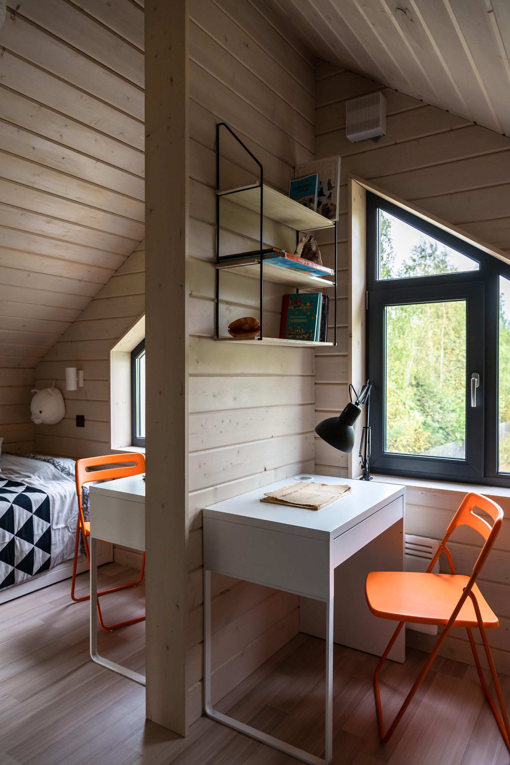 A modern kid's bedroom with tongue and groove wood siding, a white desk, black light, and orange chair.