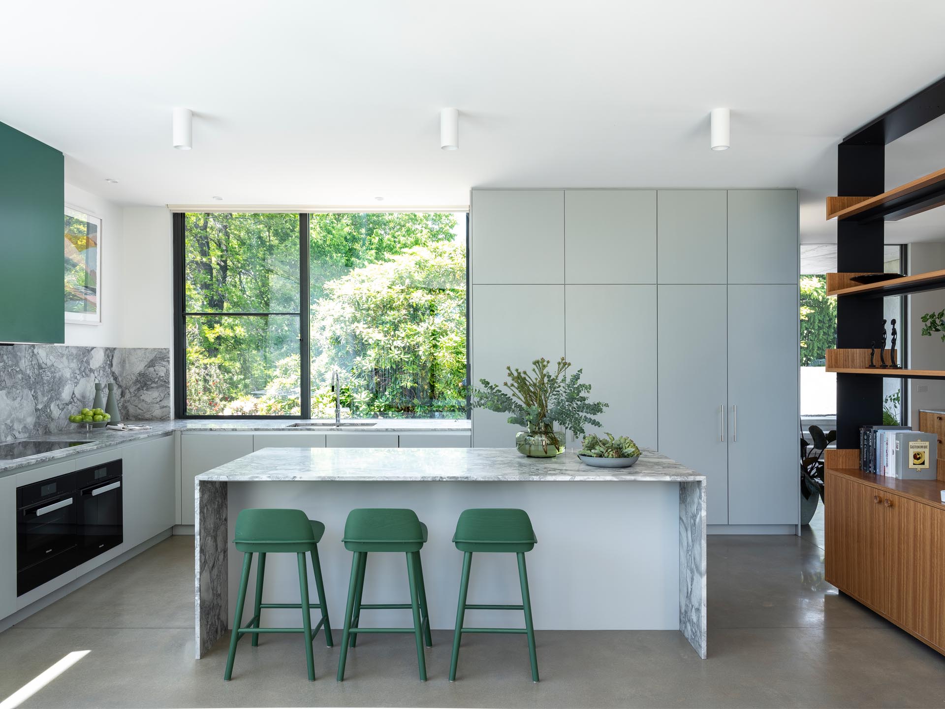 This kitchen has minimalist light gray cabinets that complement the marble countertops and concrete floors, while green accents add a pop of color.