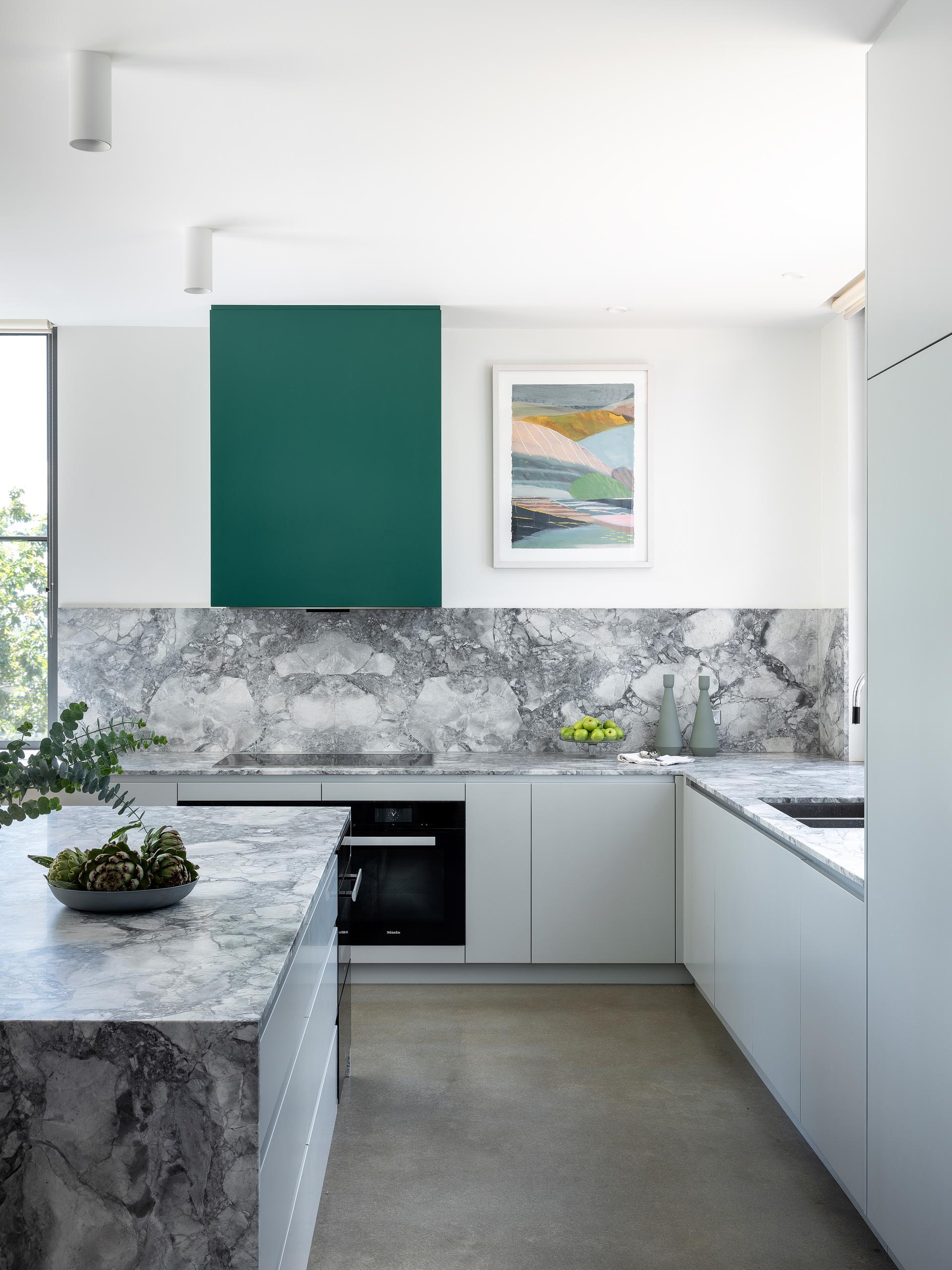 This kitchen has minimalist light gray cabinets that complement the marble countertops and concrete floors, while green accents add a pop of color.