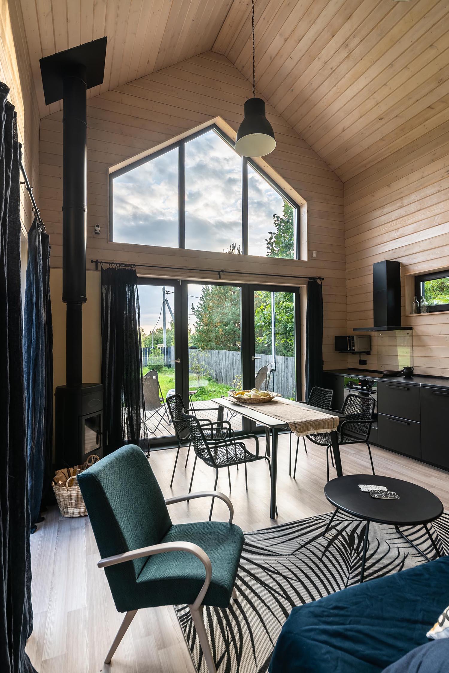 A modern barn-inspired open plan dining area and kitchen with tongue and groove wood siding and black accents, like the kitchen cabinets, the fireplace, the curtains, and furniture.