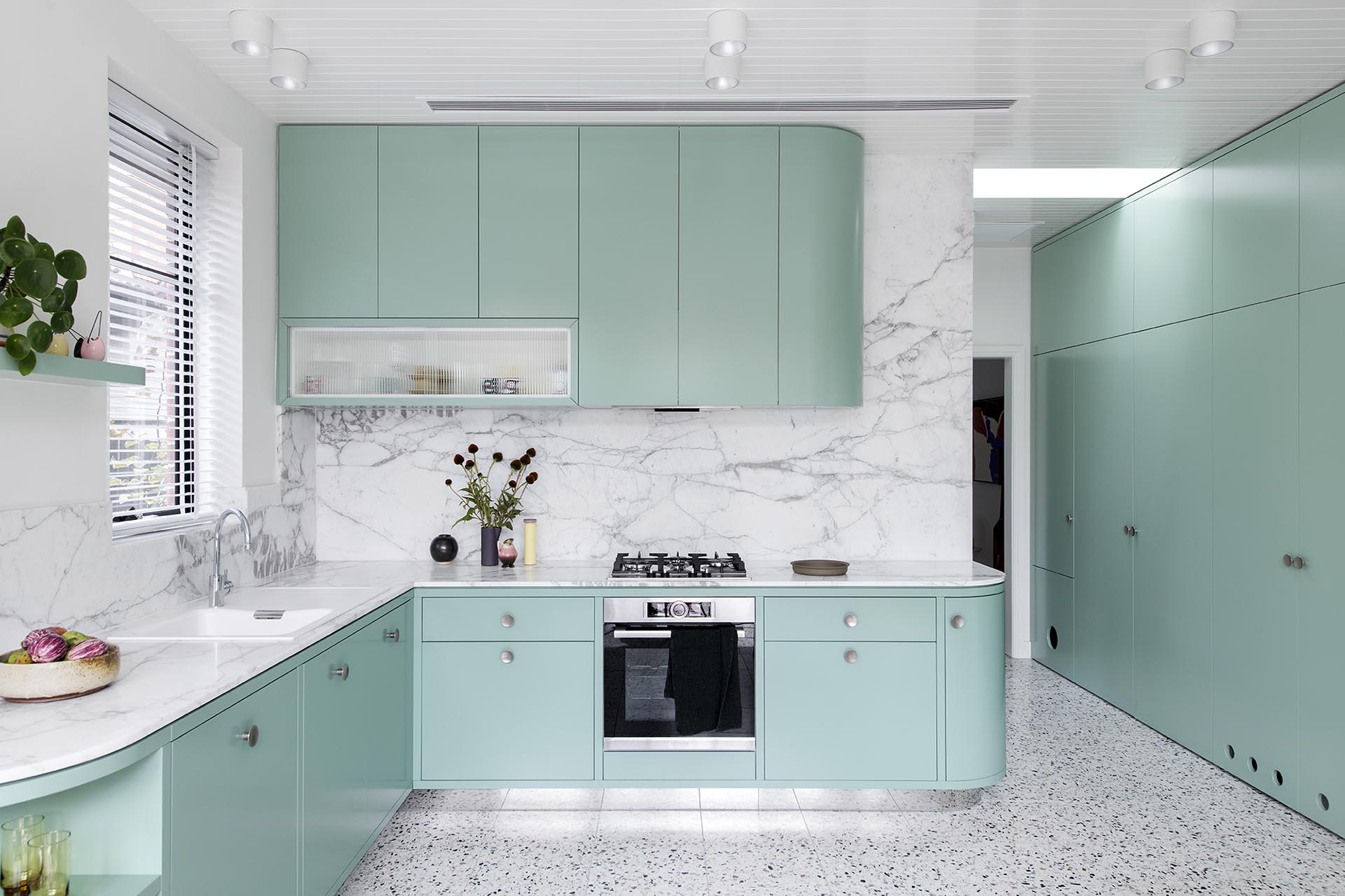 A modern mint green kitchen with Calacatta Statuario countertops, Terrazzo flooring, and white walls and ceiling.