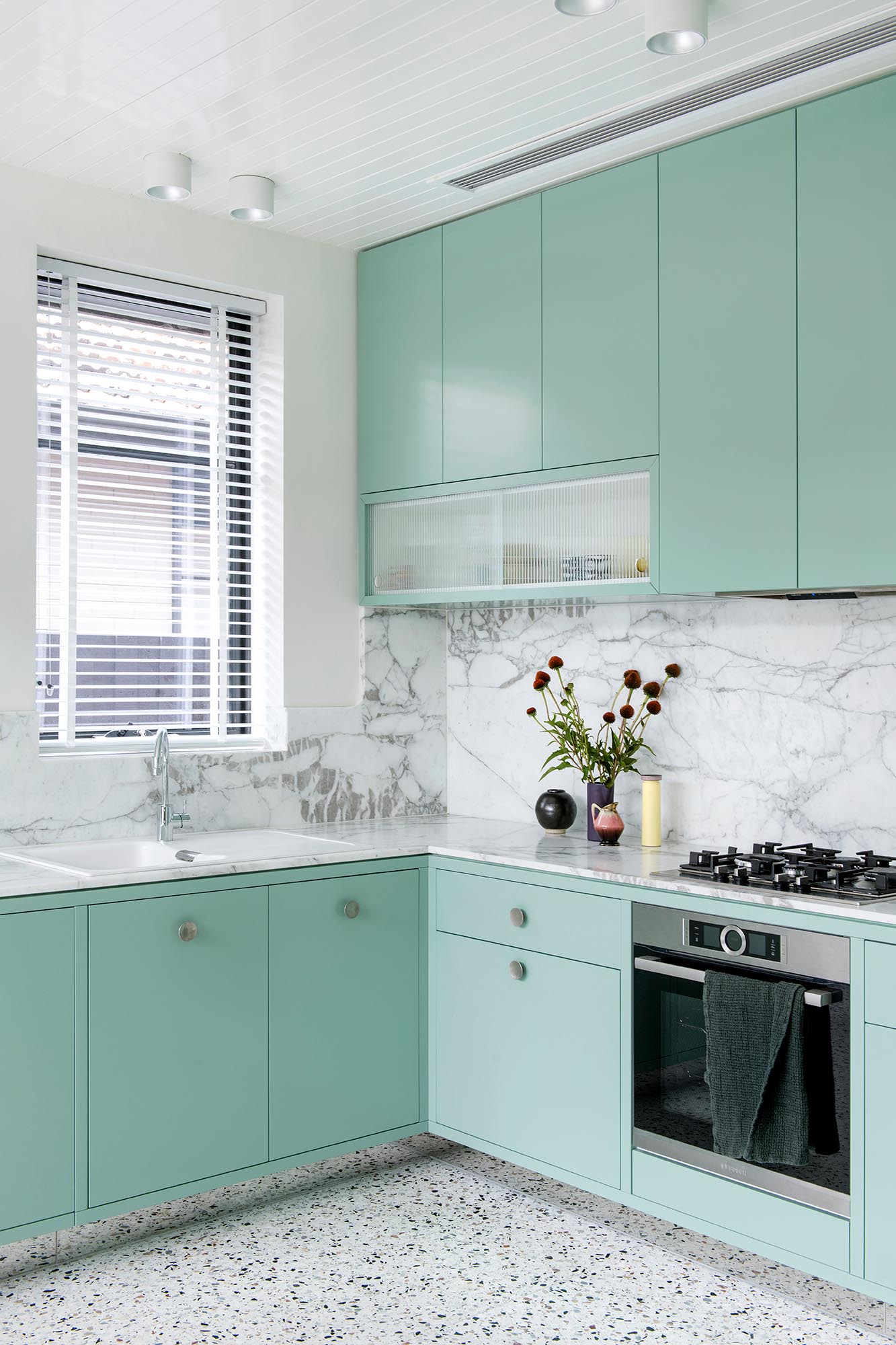 A modern mint green kitchen with Calacatta Statuario countertops, Terrazzo flooring, and white walls and ceiling.