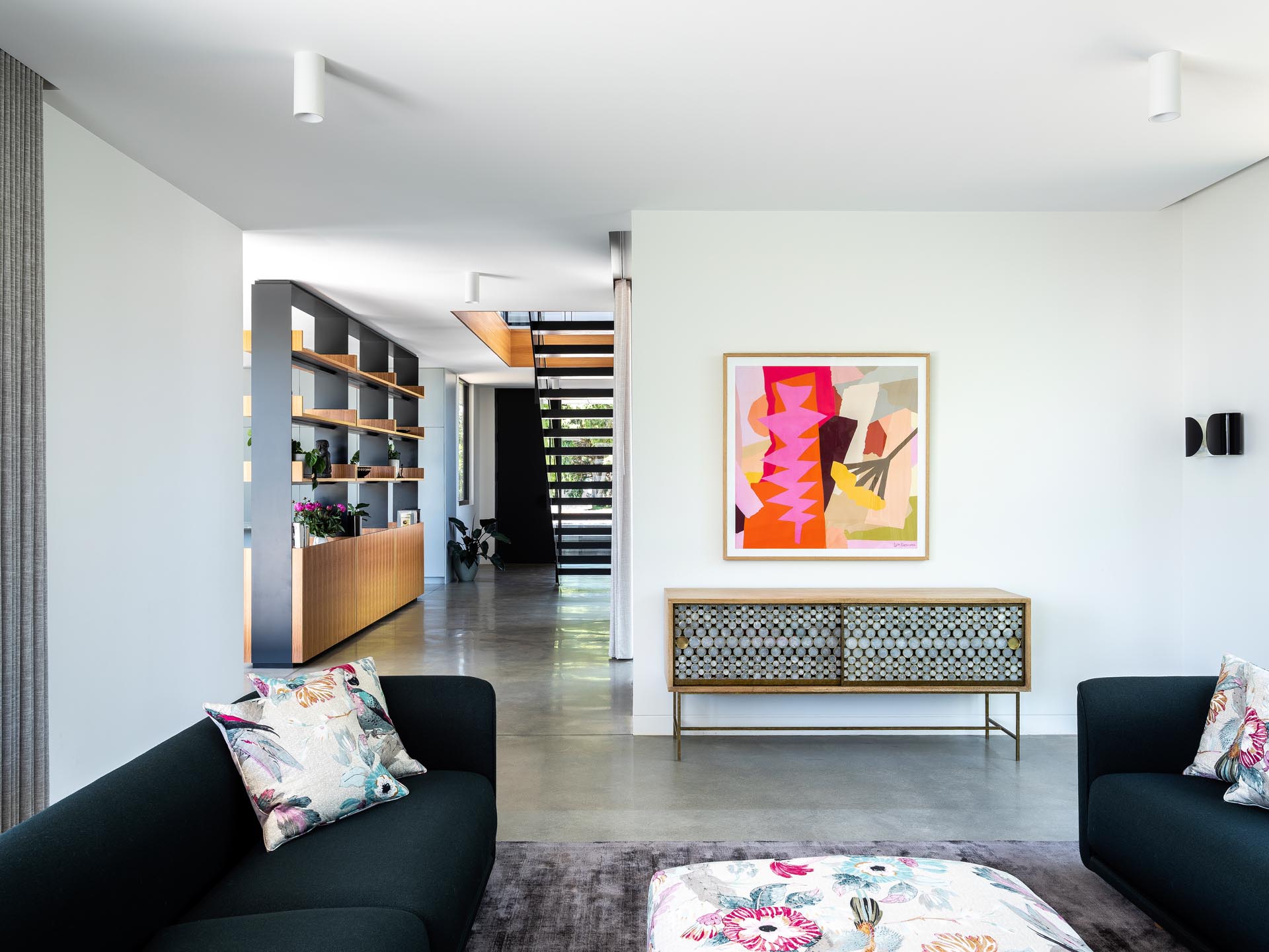 One design element found in the interior of this modern home, is an open shelving unit that separates the entryway and hallway from the living, dining, and kitchen areas.