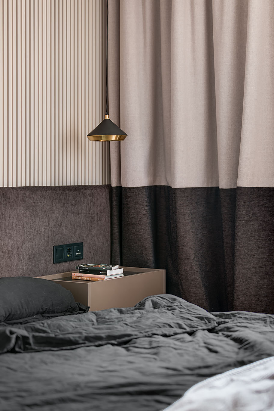 A two-tone bedroom includes different shades of chocolate and beige, a textured accent wall made from plaster, and two-tone curtains.