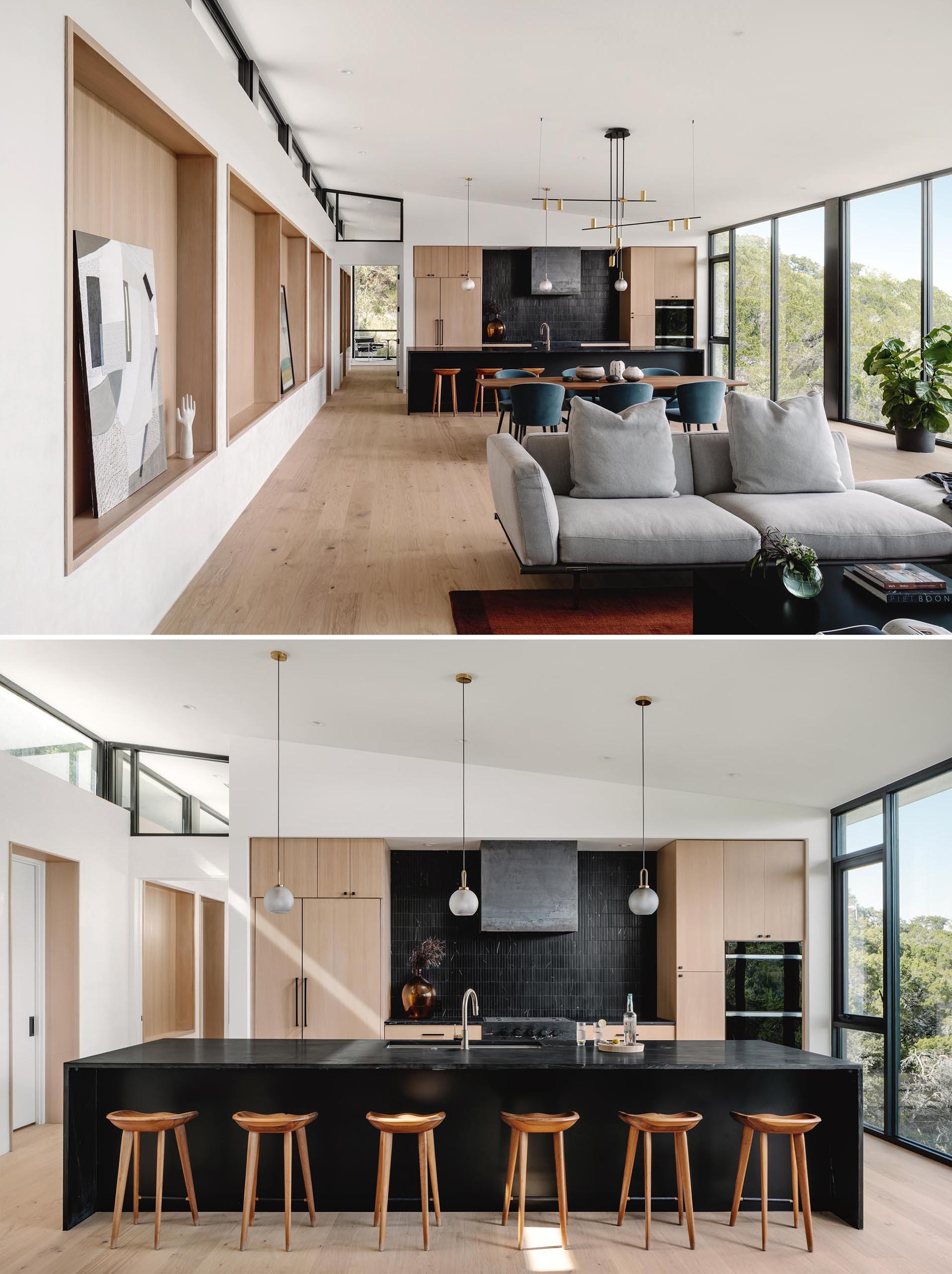 Wood-lined recessed shelving niches line the wall, while the kitchen includes light wood cabinets and a large black kitchen island that matches the black tiled backsplash.