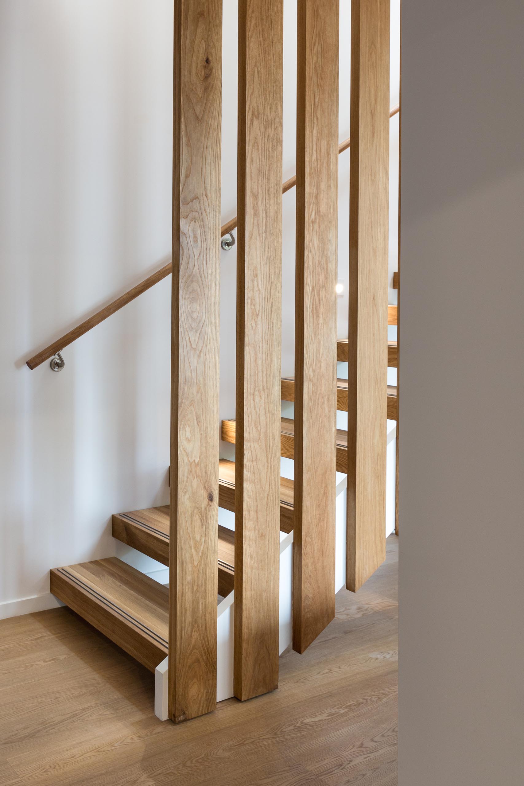 A steel and floating oak staircase with robust timber balusters and embedded stainless steel strips within the stair treads that create a non slip surface.