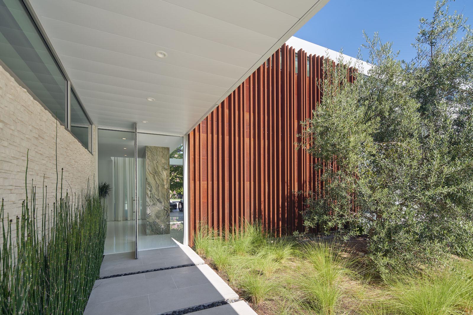 A covered walkway connects to the pivoting glass front door and the entryway.