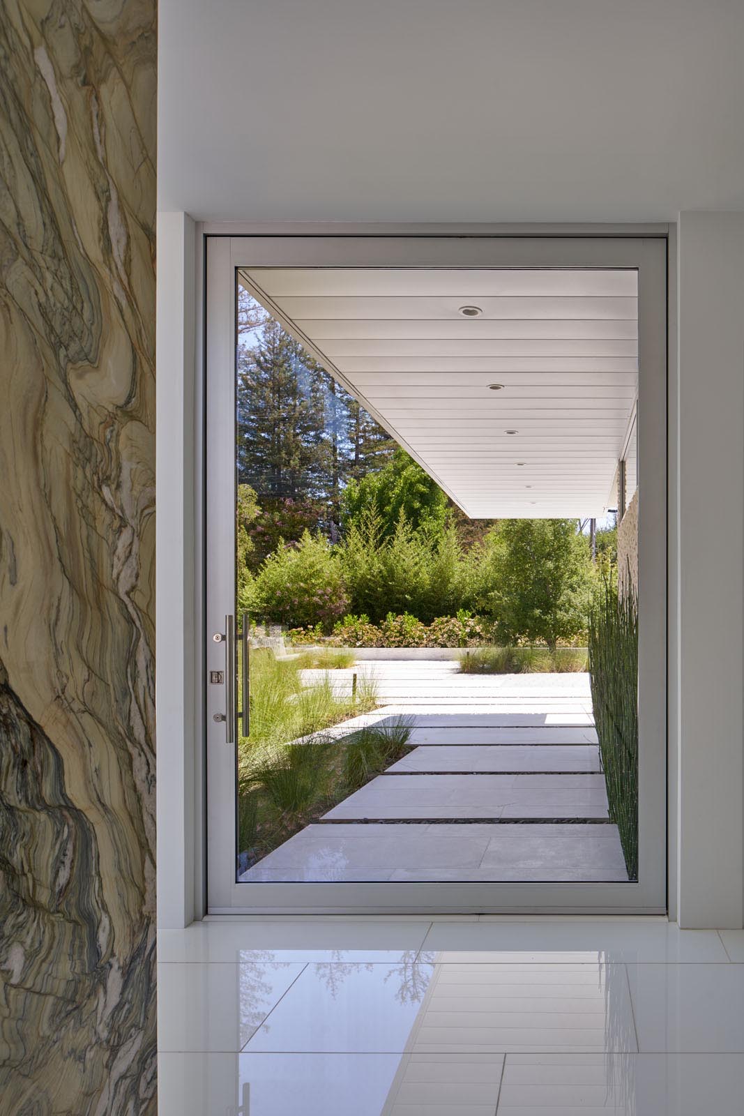 A covered walkway connects to the pivoting glass front door and the entryway.