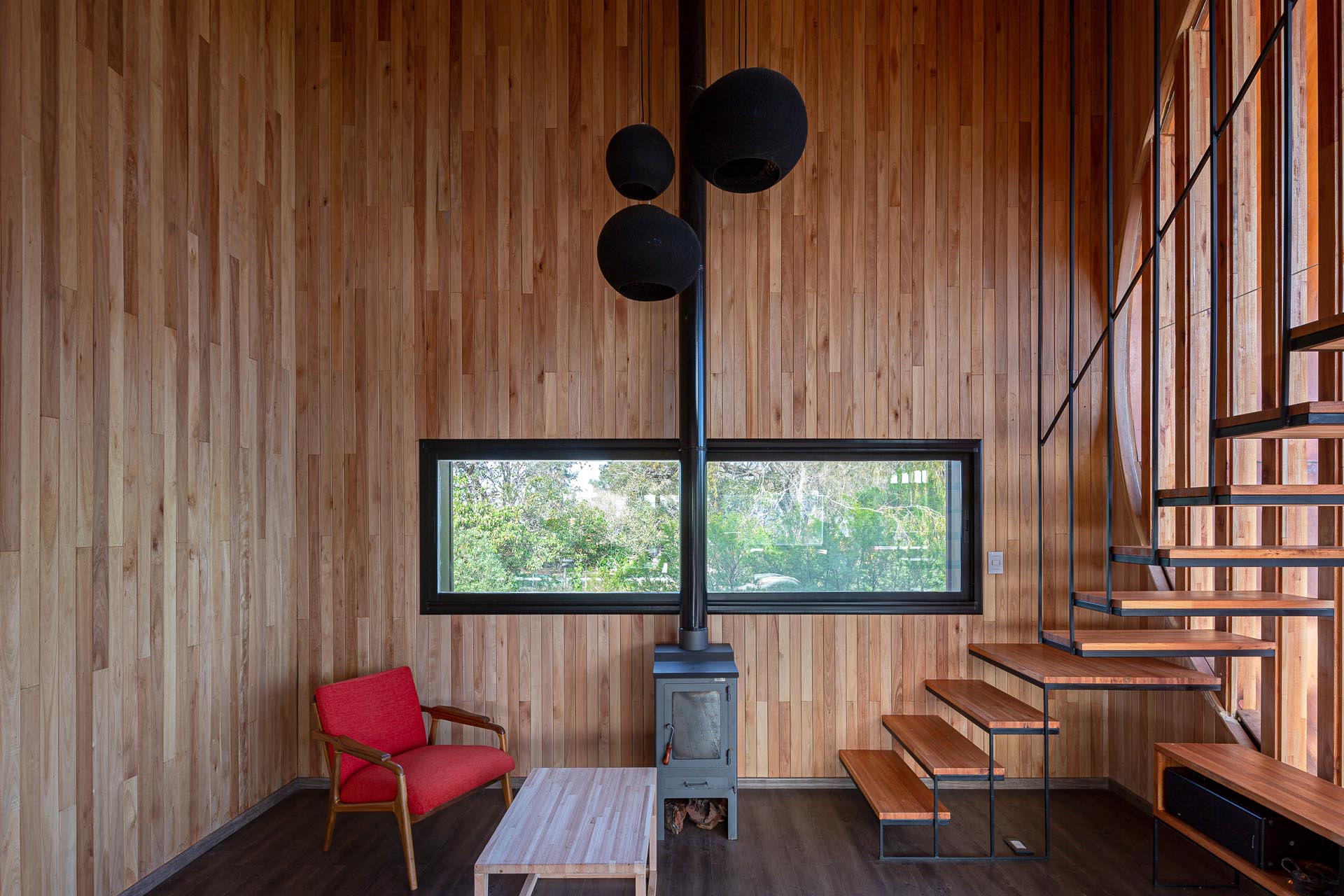 A small and modern house with a wood-lined interior, and a black fireplace that matches the window frames.