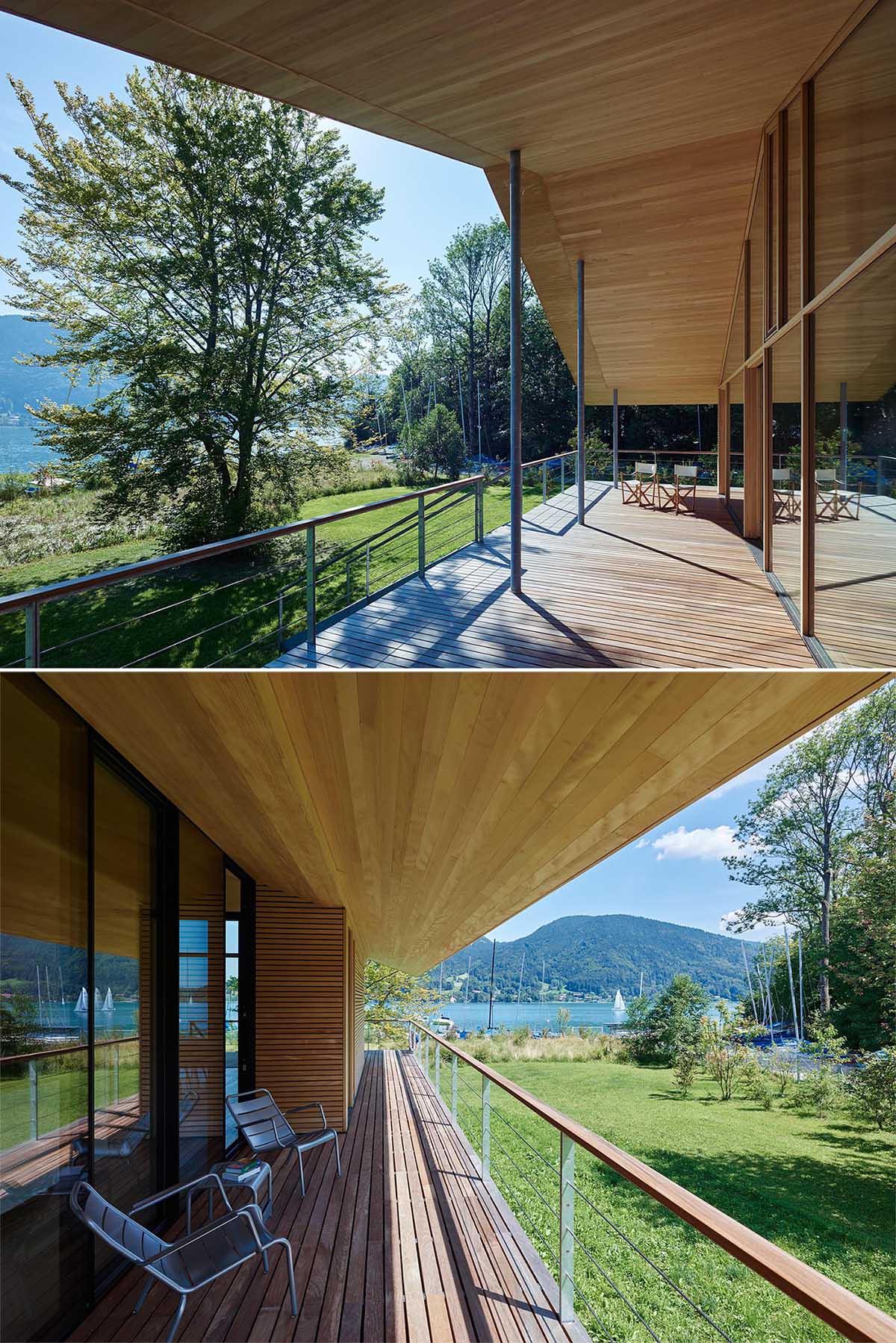 A wooden walkway surrounds this modern house and widens into a terrace at the lakeside, completely covered by the steep saddleback roof.