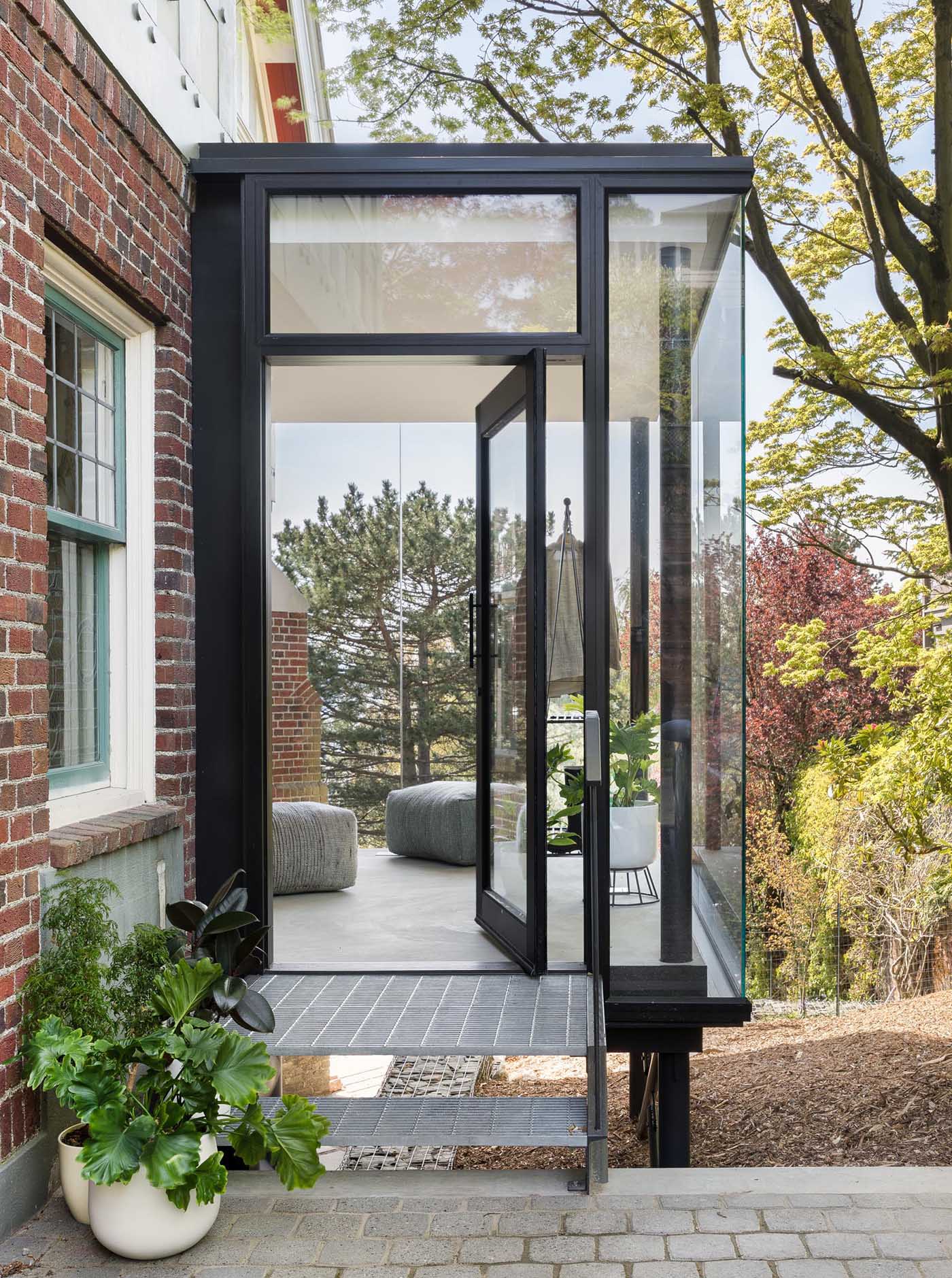 This updated light filled home has a new glass enclosed entryway with black frames, creating a contemporary addition to the brick and wood house.