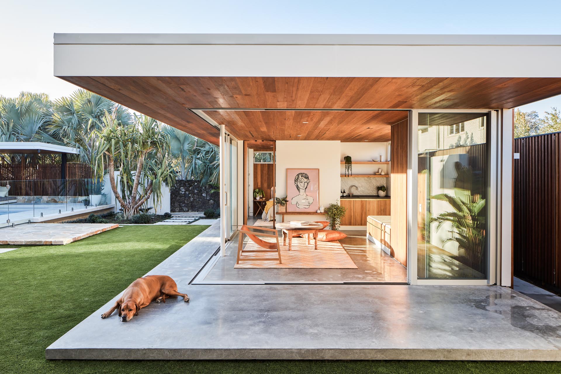 With mid-century modern influences, the sliding glass walls of this backyard studio, seamlessly open the interior spaces of the studio to the backyard. Inside, there's a wood ceiling, polished concrete floors, a small bench, storage, and a kitchenette.