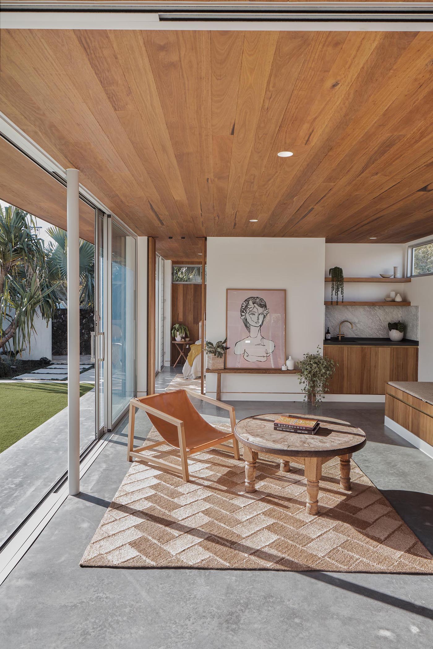 With mid-century modern influences, the sliding glass walls of this backyard studio, seamlessly open the interior spaces of the studio to the backyard. Inside, there's a wood ceiling, polished concrete floors, a small bench, storage, and a kitchenette.