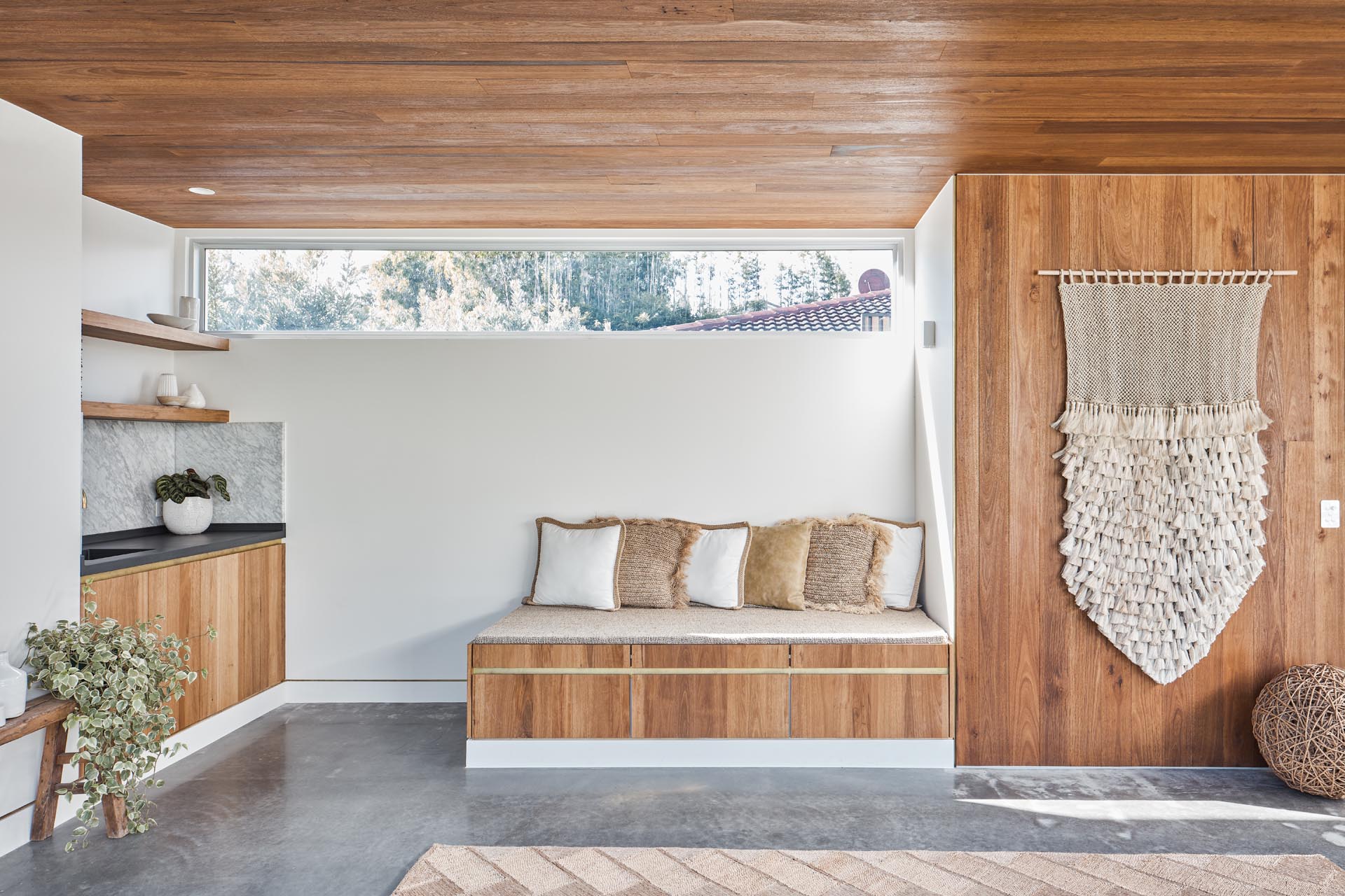 With mid-century modern influences, the sliding glass walls of this backyard studio, seamlessly open the interior spaces of the studio to the backyard. Inside, there's a wood ceiling, polished concrete floors, a small bench, storage, and a kitchenette.