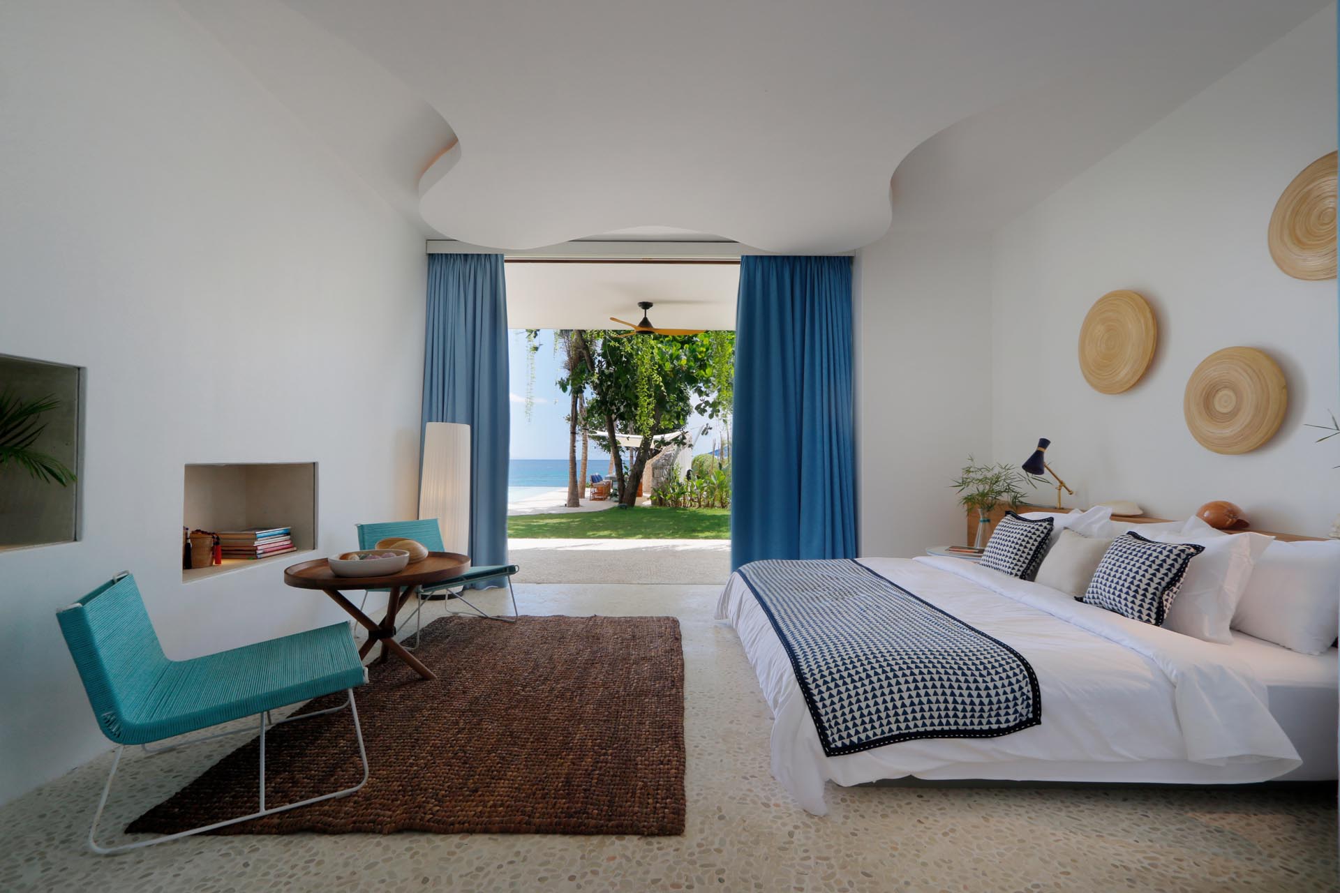 A modern beach house bedroom opens to the outdoors, and has blue accents.